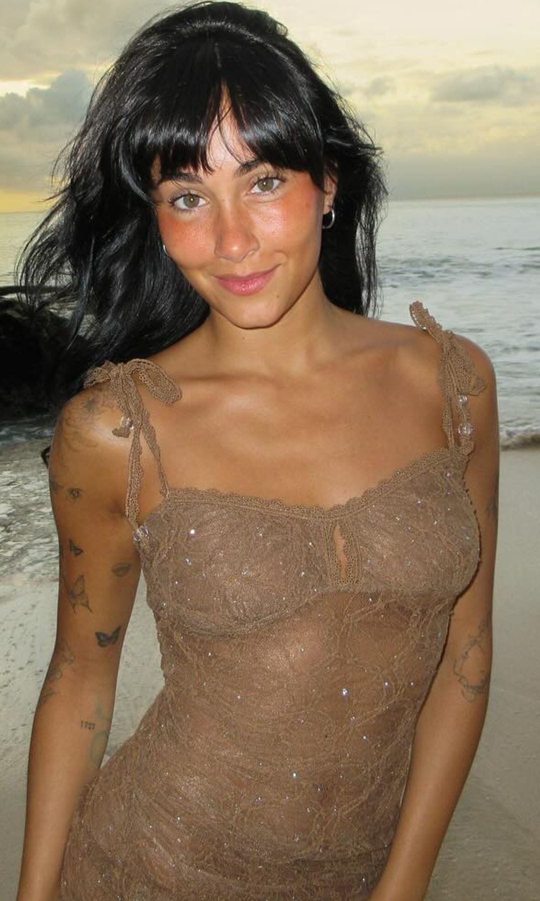Aitana con vestido semitransparente en la playa con tatuajes en el brazo