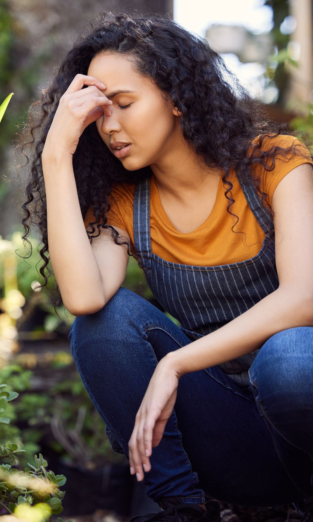 mujer rodeada de plantas cansada, con la mano en la cabeza y los ojos cerrados