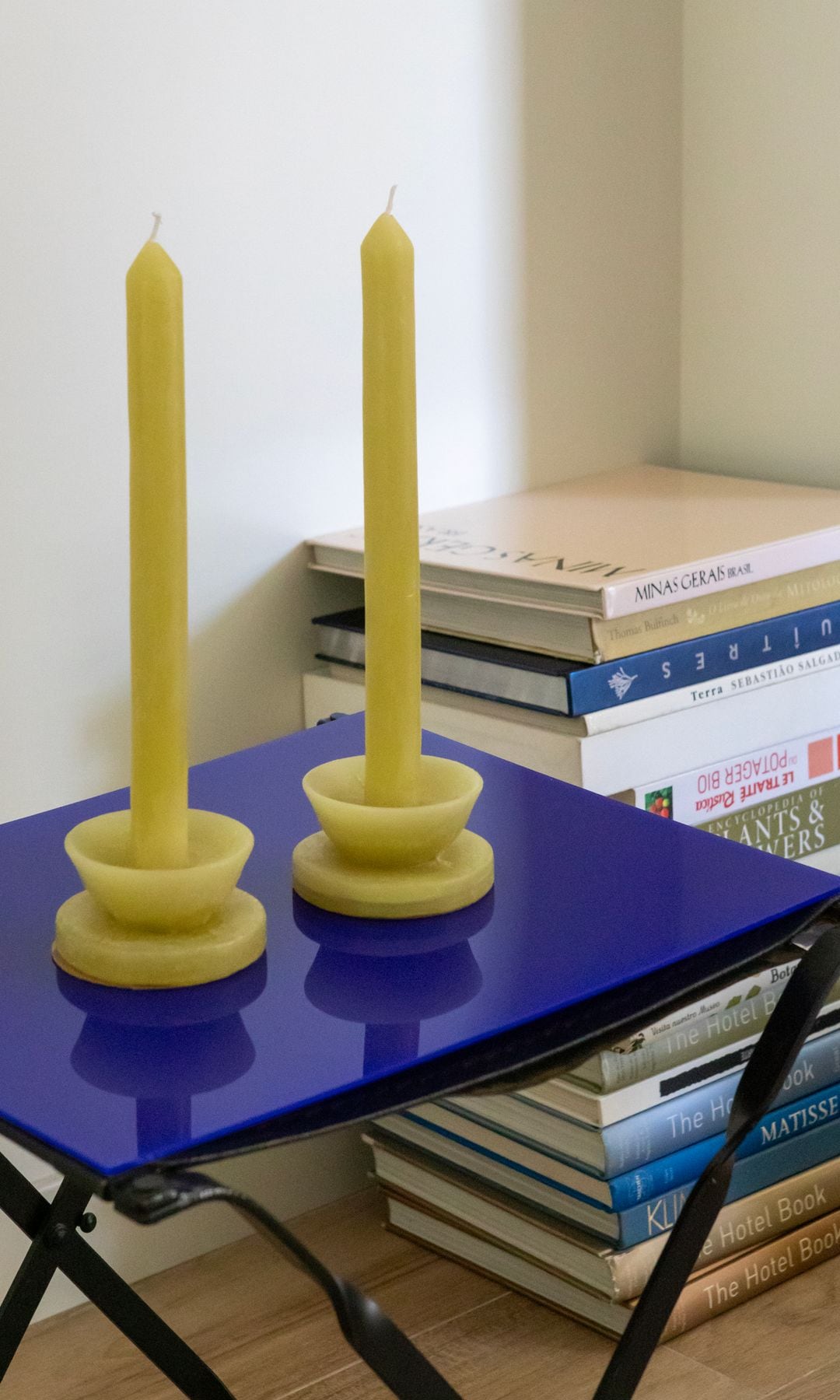 Rincón con mesa auxiliar azul Klein, velas candelabro amarillas y columna de libros en el suelo