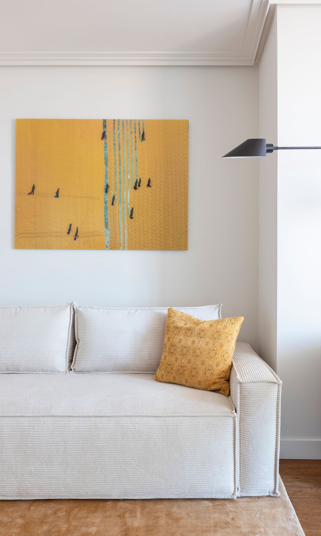 Salón con sofá blanco, cuadro amarillo en la pared, cojines, suelo de madera