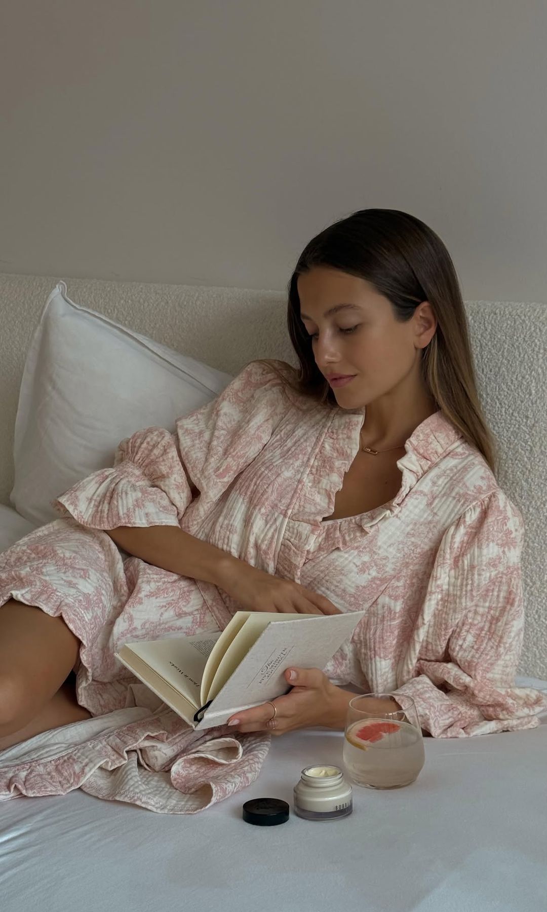 La modelo y actriz Zoe Pastelle con un libro, una infusión y su crema hidratante con bata en la cama