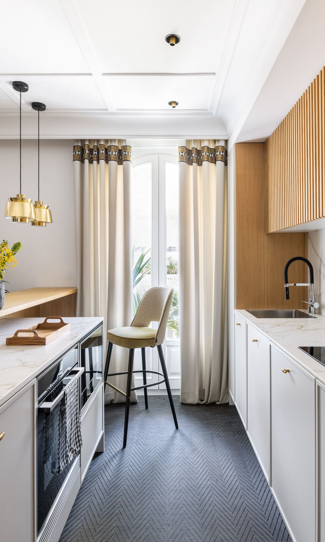 Cocina alargada con muebles de madera y blancos, suelo negro, barra alta para comer con taburete 