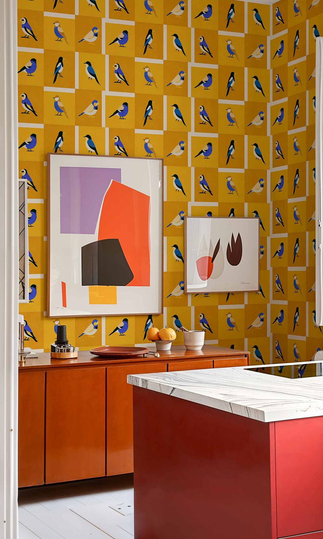 Cocina con muebles rojos, encimera blanca, papel pintado de color amarillo, cuadros y aparador de madera