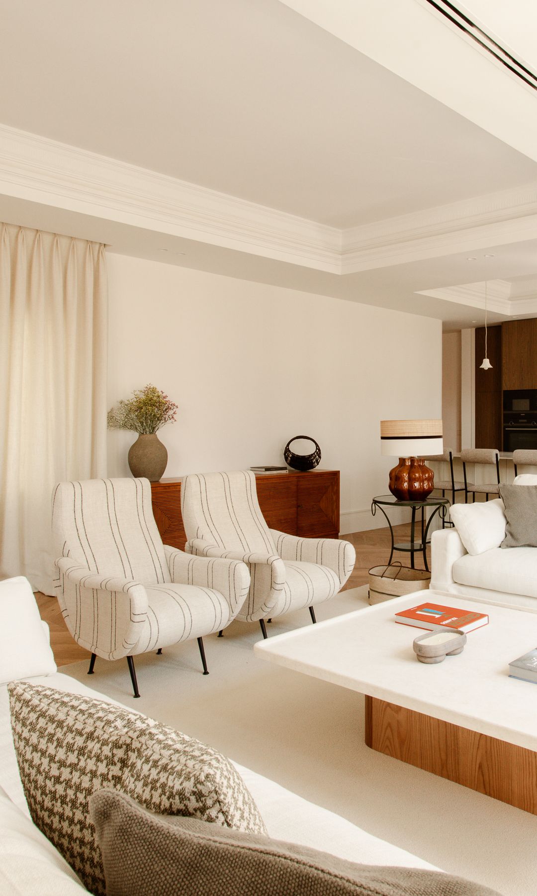 Salón con mesa de centro de madera con el sobre blanco, alfombra, butacas tapizadas 