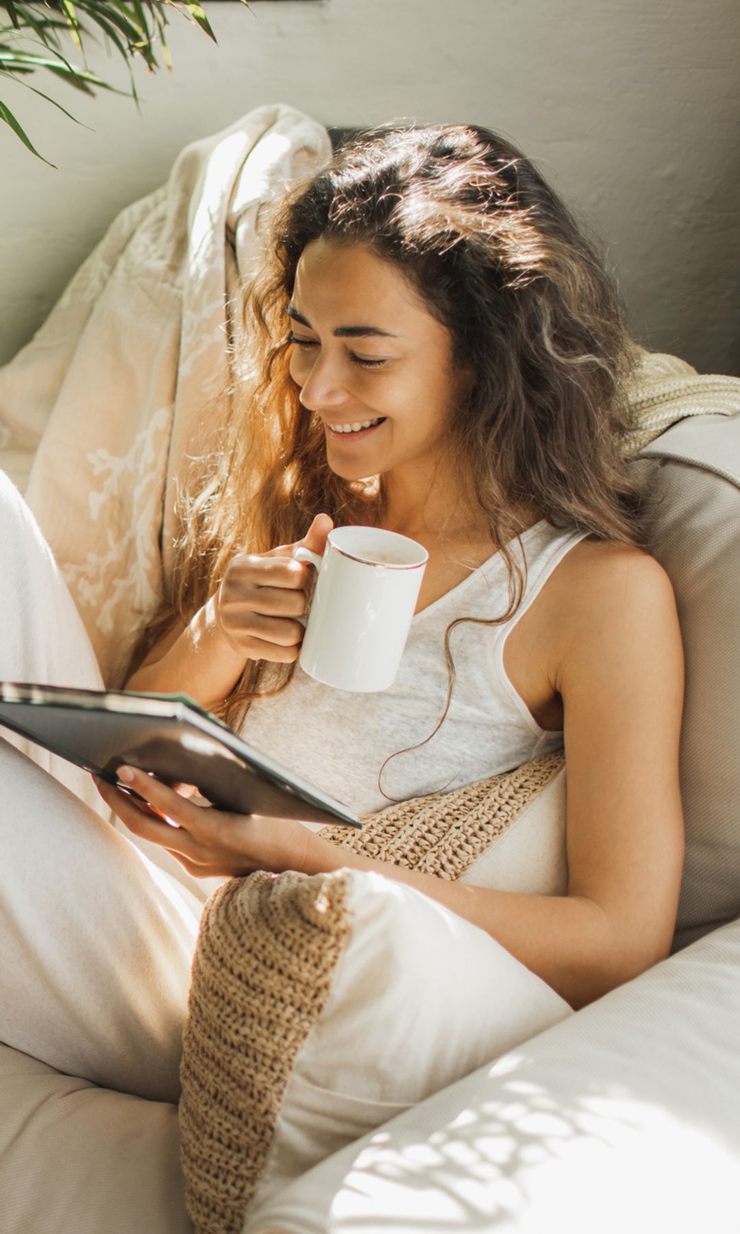 Mujer con una taza de café, leyendo feliz en el sofá