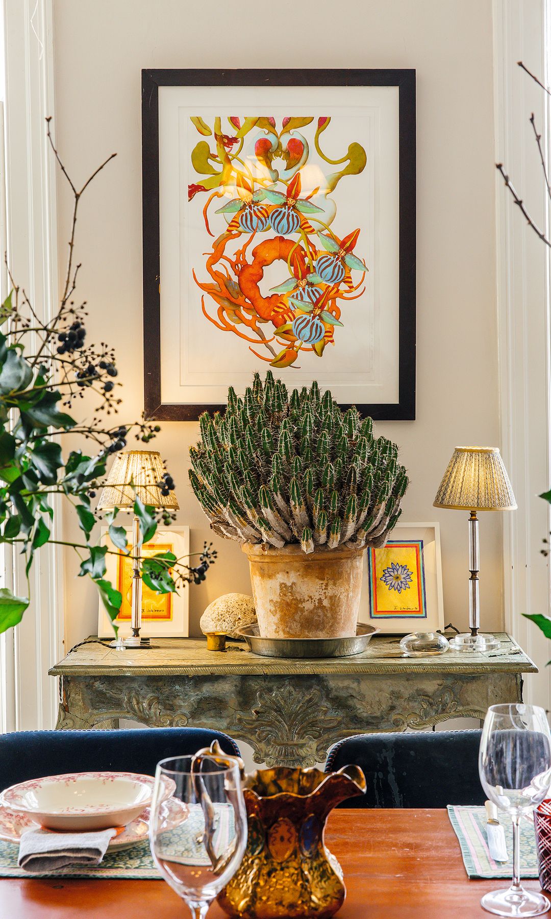 Comedor elegante con pintura abstracta, cactus grande y mesa lista para cenar