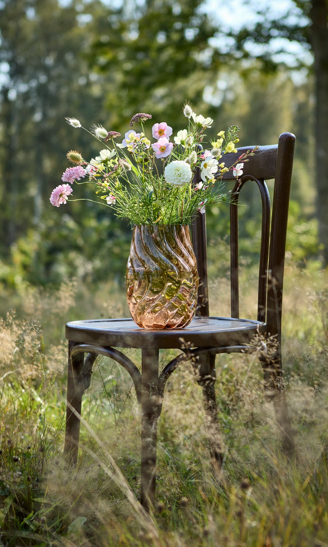 Silla en el campo con jarrón de cristal amarillo y flores
