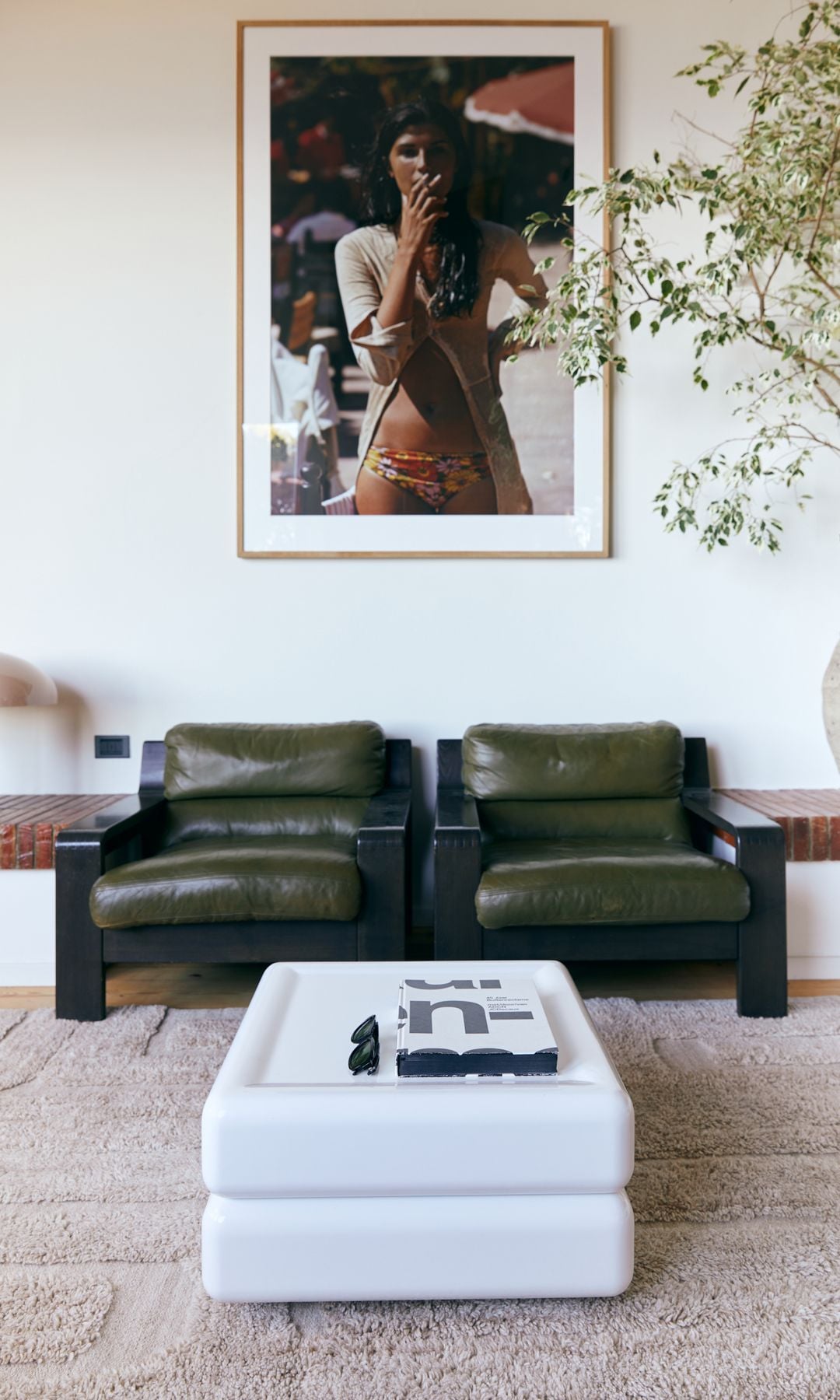 Salón con sofá de cuero verde, alfombra, mesa de centro blanca y fotografía Xl en la pared del sofá