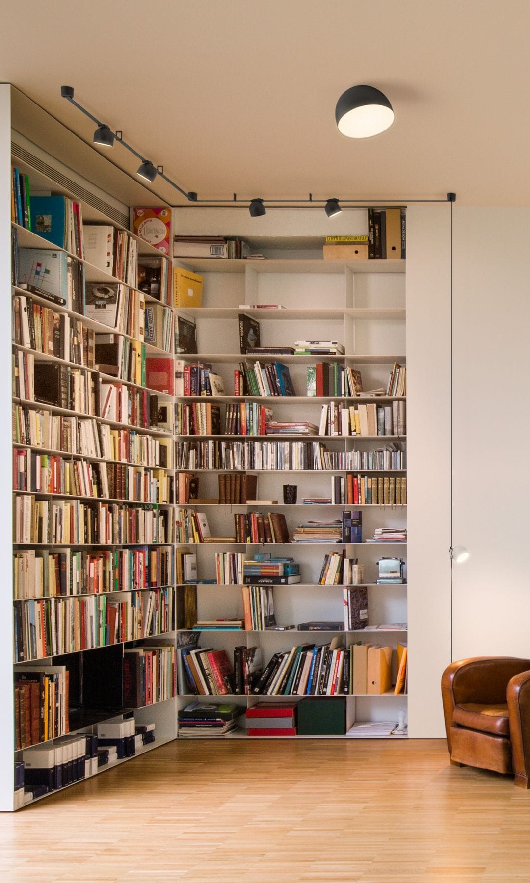 Rincón de lectura con librería de suelo a techo, focos iluminando, sofá de cuero, lámpara de techo, tipo plafón negro