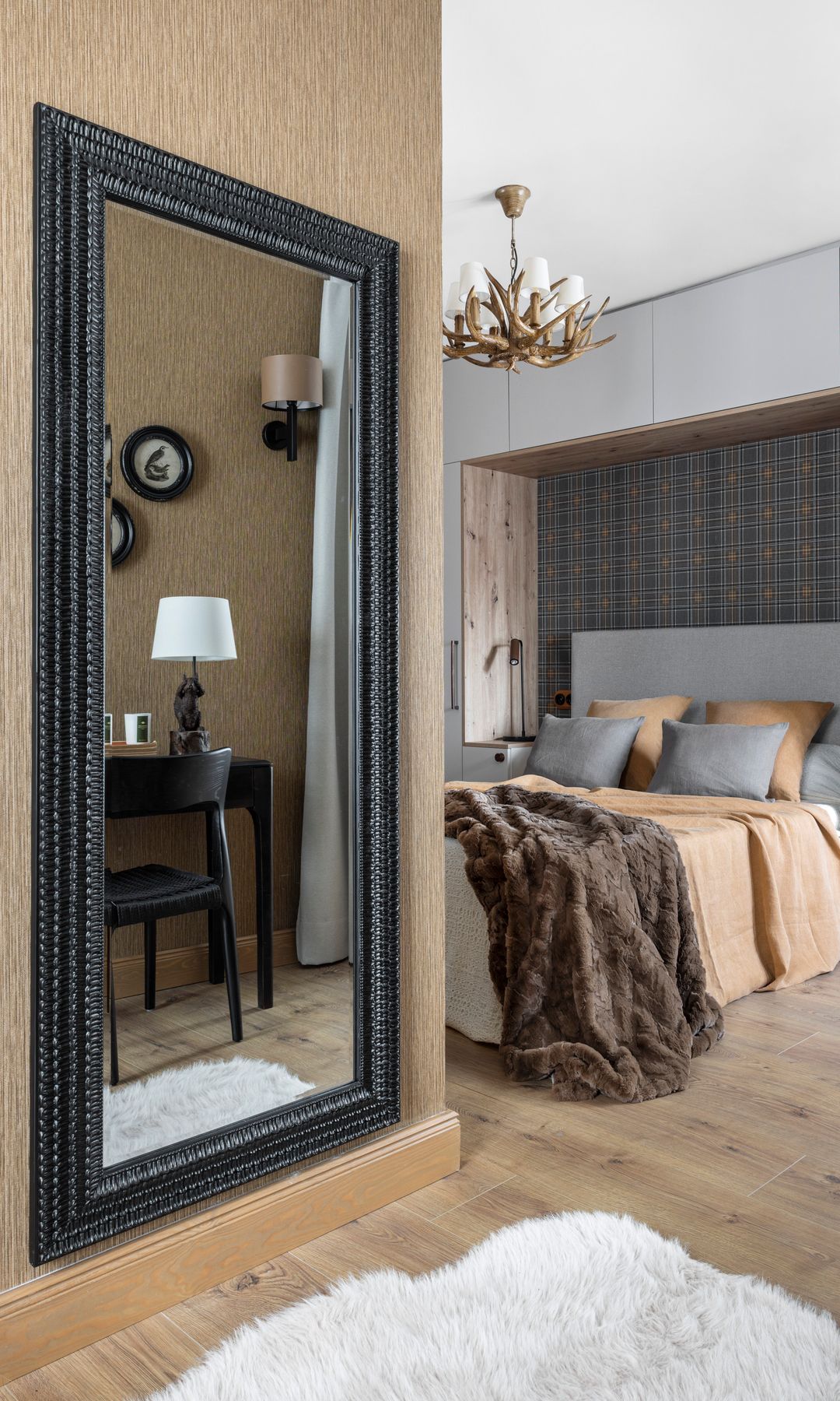 Dormitorio con cabecero tapizado en gris, cama con cojines, espejo XL colgado en la pared con el marco negro 