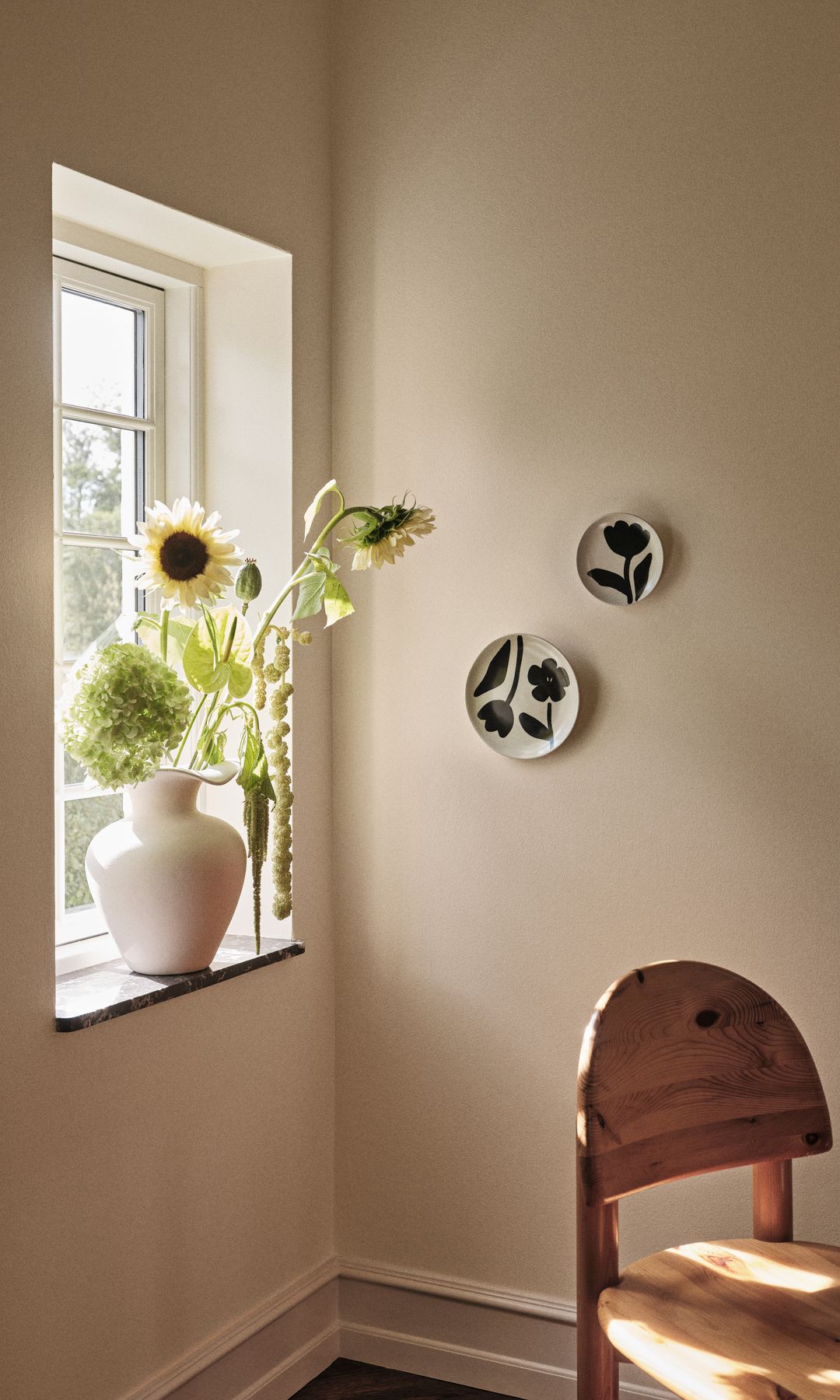 Rincón con ventana, jarrón con girasoles, platos en la pared, silla de madera