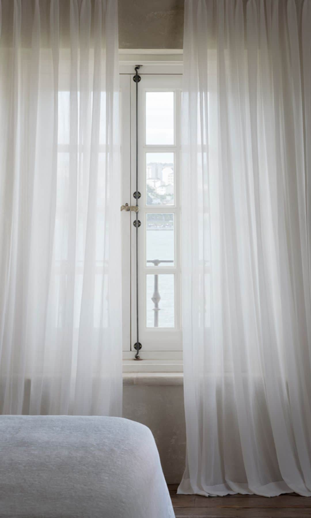 Dormitorio con visillos blancos, ventana con el marco blanco, ropa de cama blanco, escultura