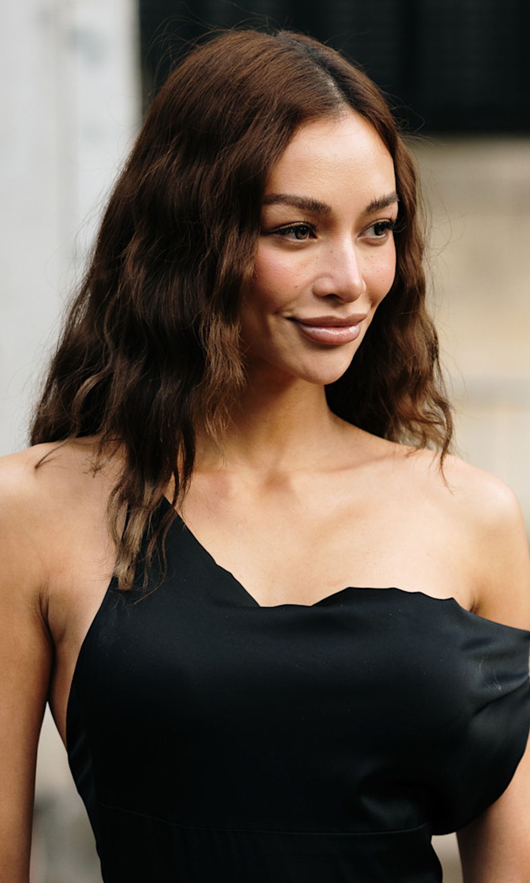 Chica con pelo rizado y castaño oscuro, vestido asimétrico negro en la Semana de la Moda de París