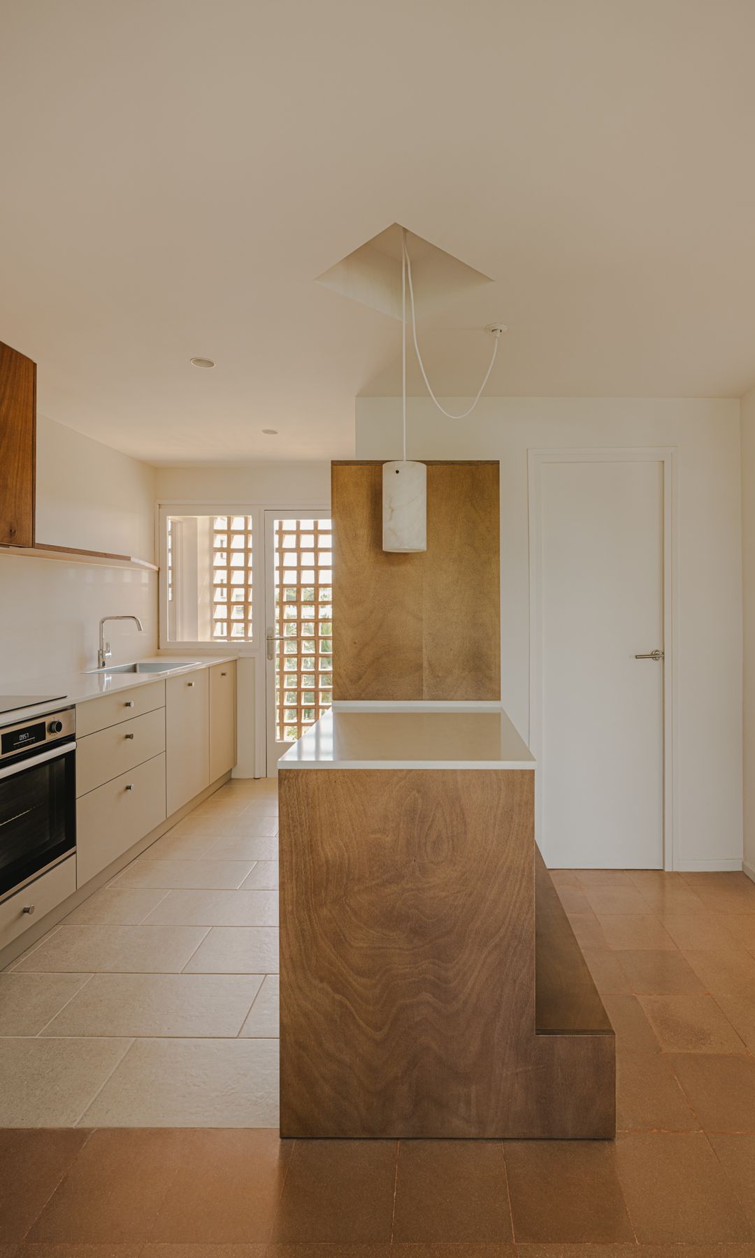 Cocina abierta con isla, con puerta corredera que la separa del dormitorio, suelo blanco, muebles blancos y de madera 