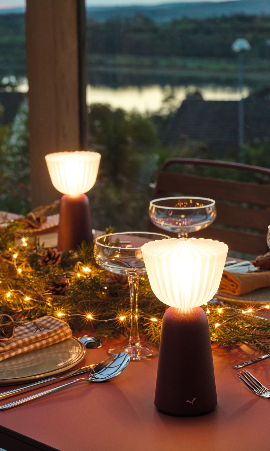 Mesa de exterior de noche con lámparas portátiles, copas y platos 