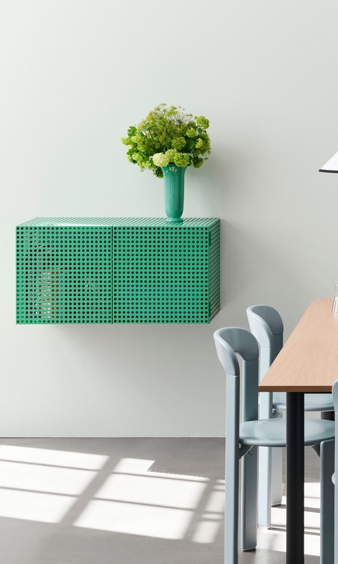 Comedor con mesa de madera y sillas grises, lámpara de techo, aparador verde metálico perforado, con jarrón