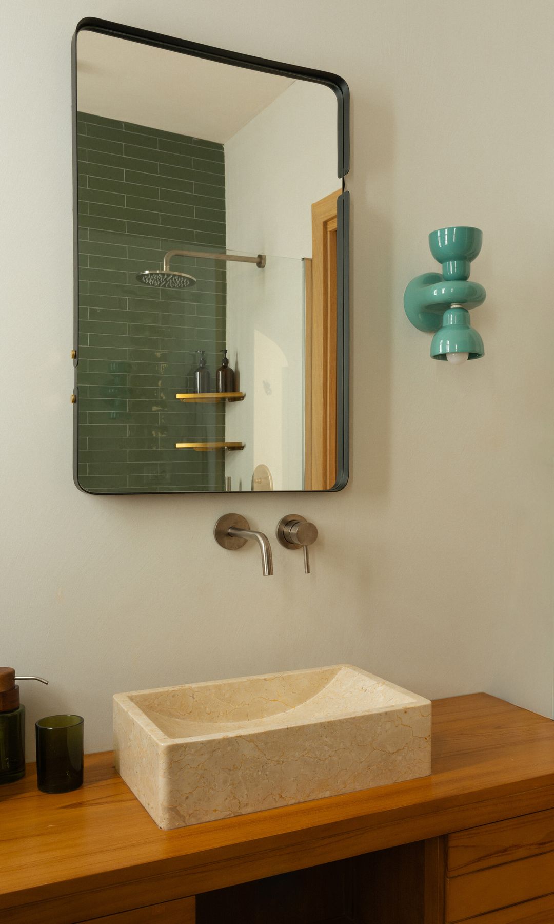 Baño con ducha, revestimiento de azulejos verdes, aplique de pared, lavabo sobre encimera, mueble de lavabo de madera, grifería dorada 