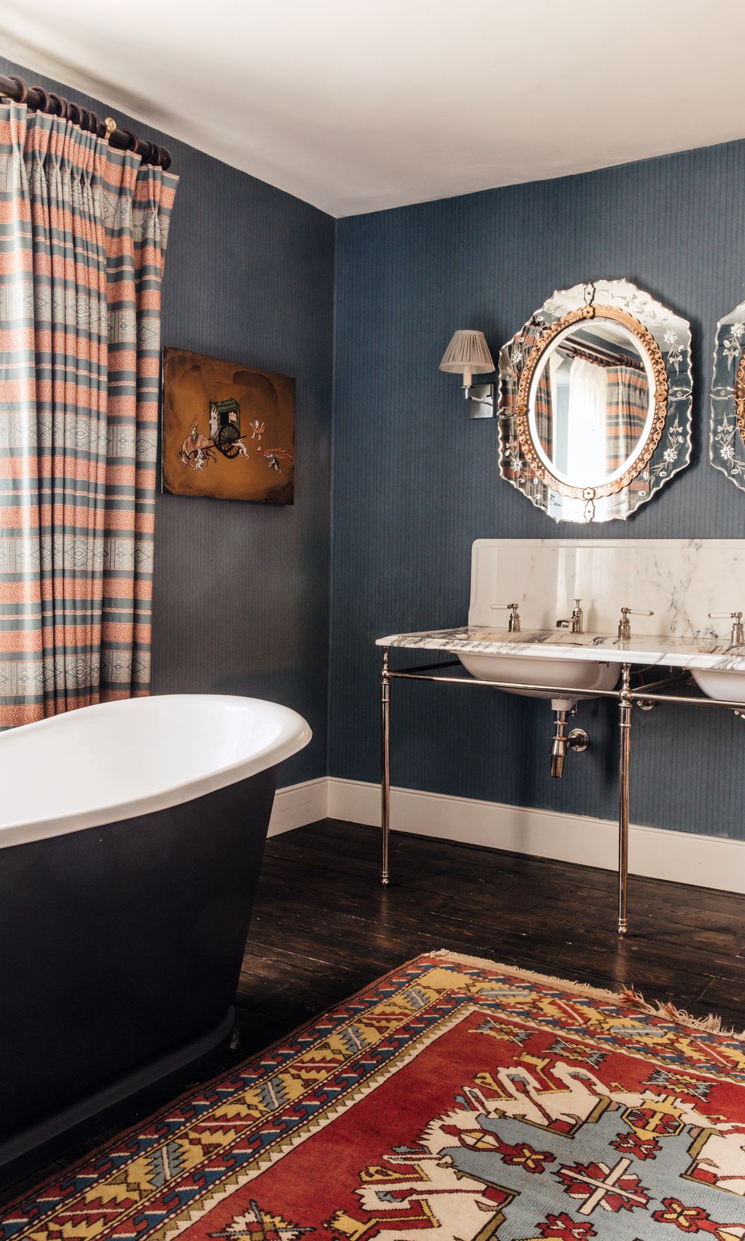 Baño elegante con bañera, doble lavabo, espejos decorativos y alfombra colorida.