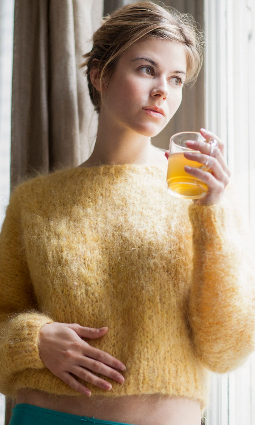 Mujer tomando vinagre de manzana y mirando por la ventana
