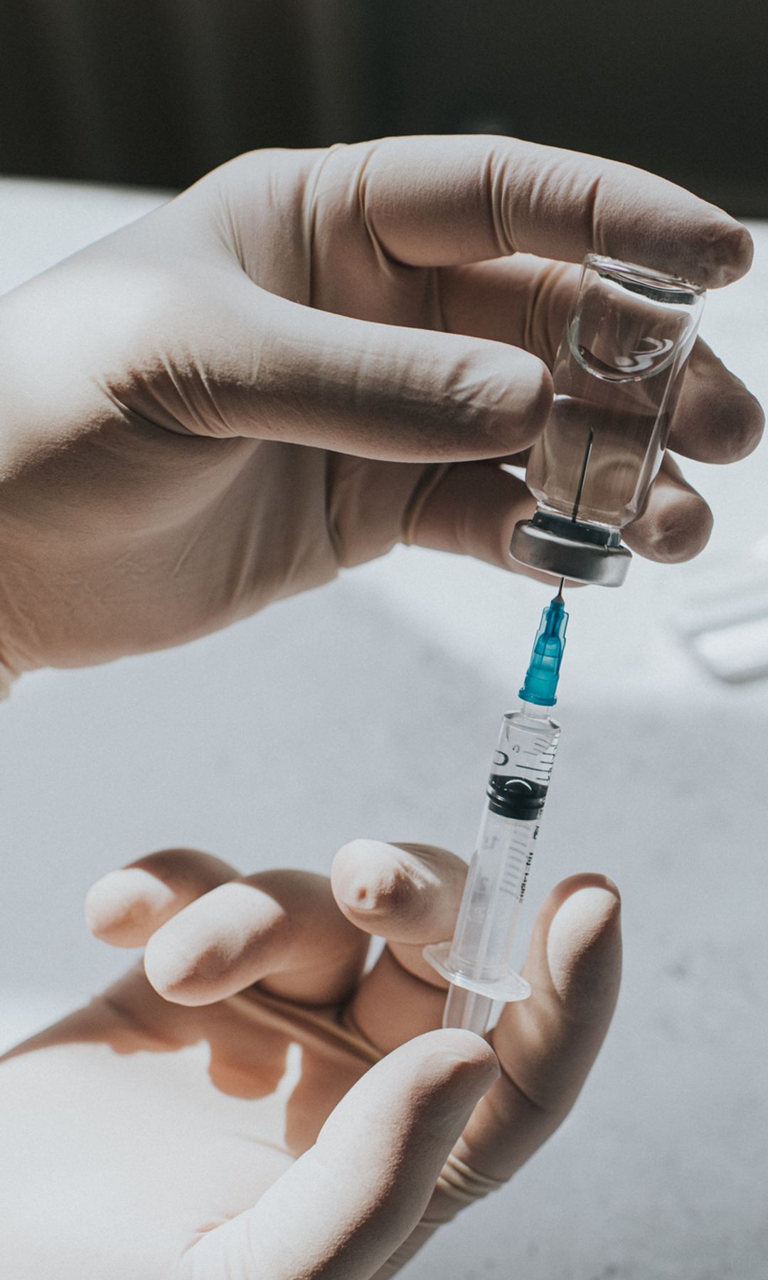 Una mano con guantes de látex sostiene un vial con un líquido transparente y una jeringa.