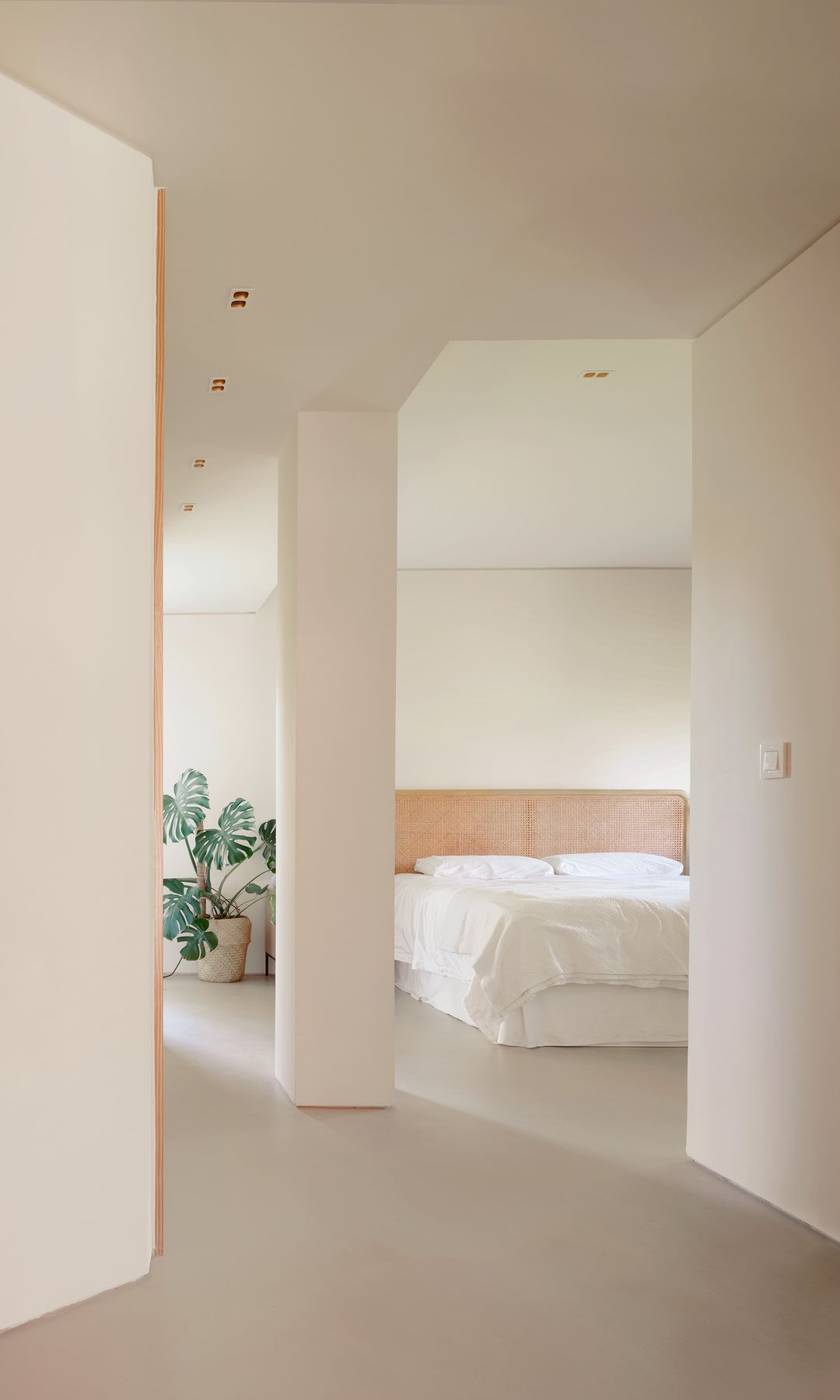 Dormitorio minimalista en blanco, con columnas blancas, puerta de madera, cabecero de rejilla