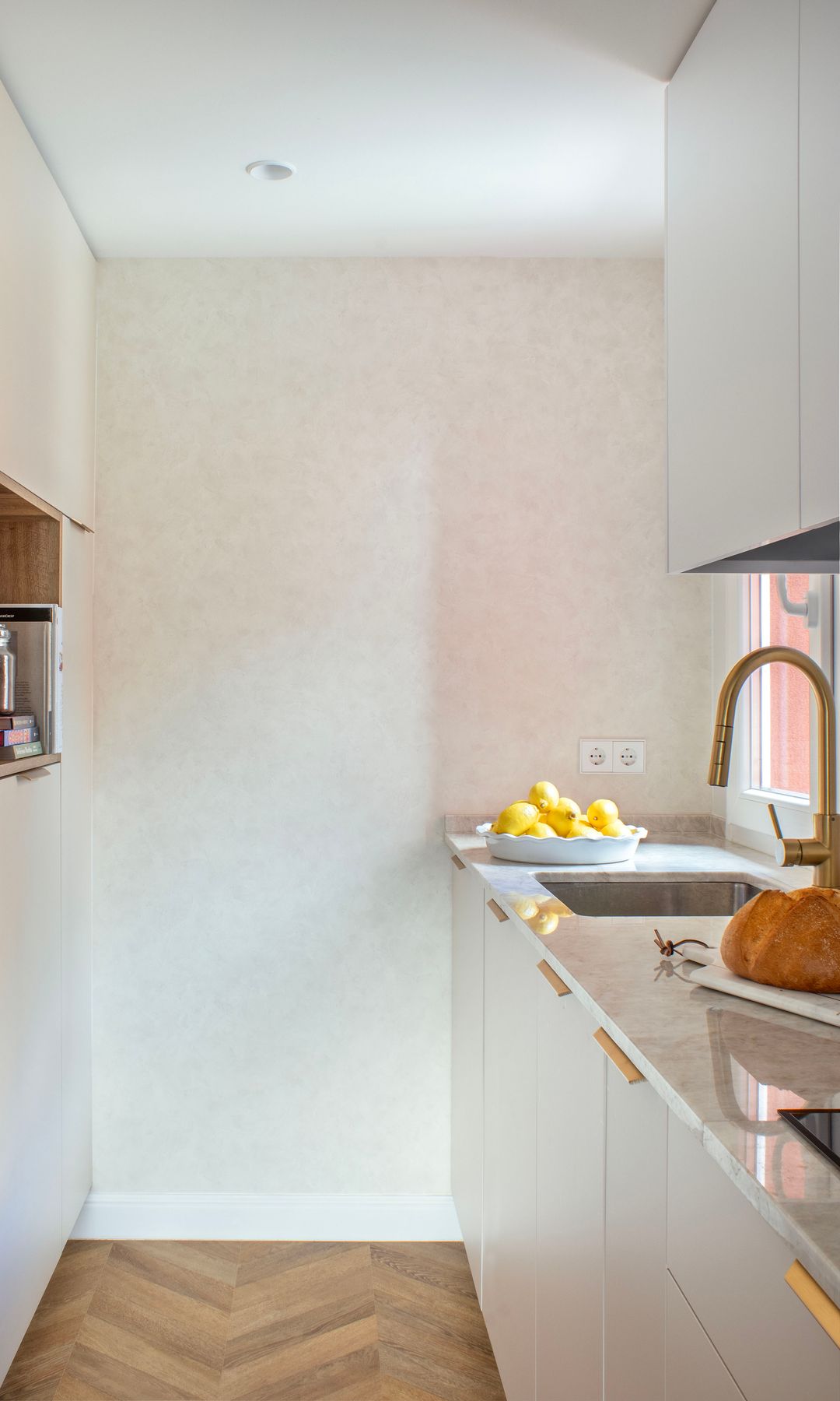 Cocina pequeña alargada de color blanco y grifería dorada 