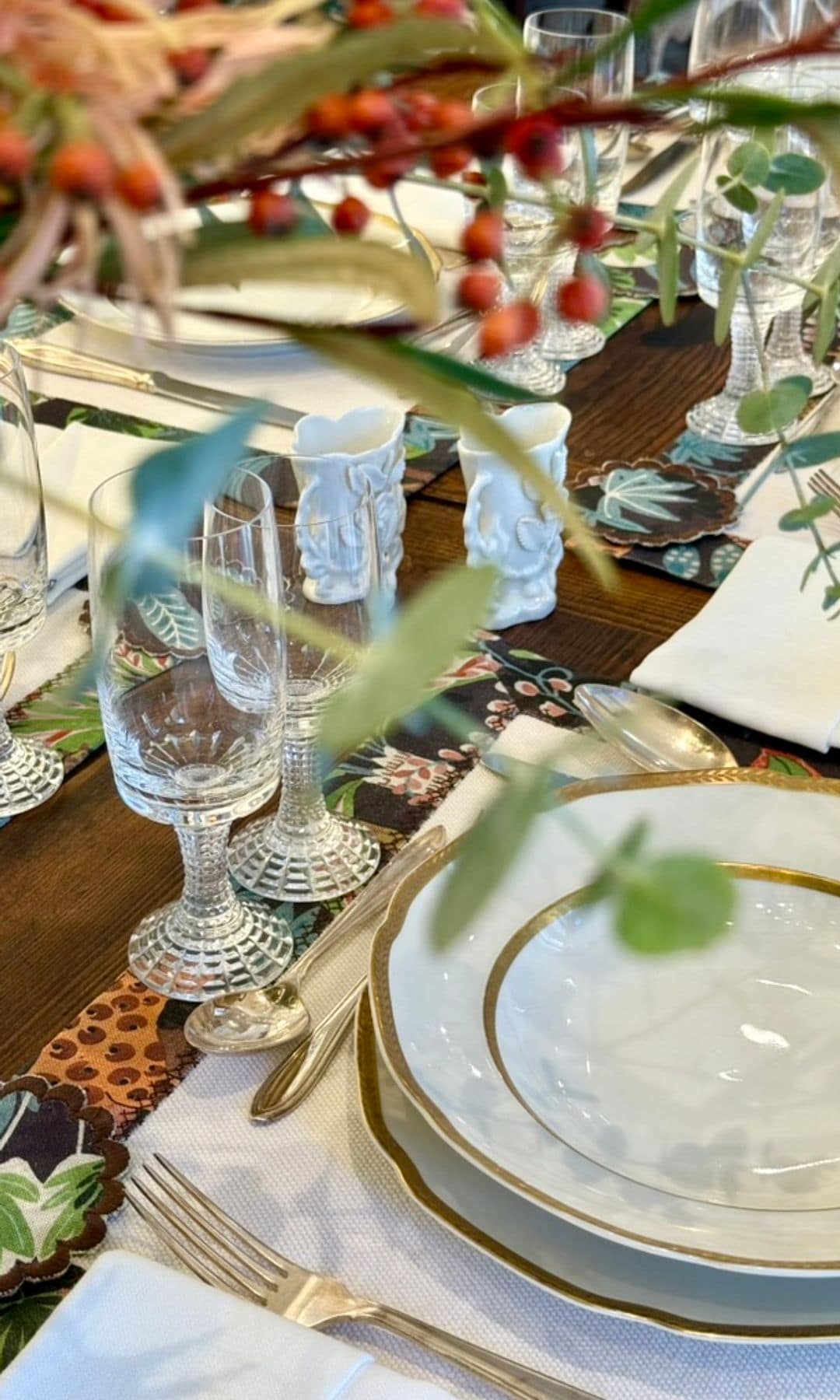 Mesa de Navidad con manteles individuales, vajilla blanca con el borde dorado, copas y centro de Navidad 