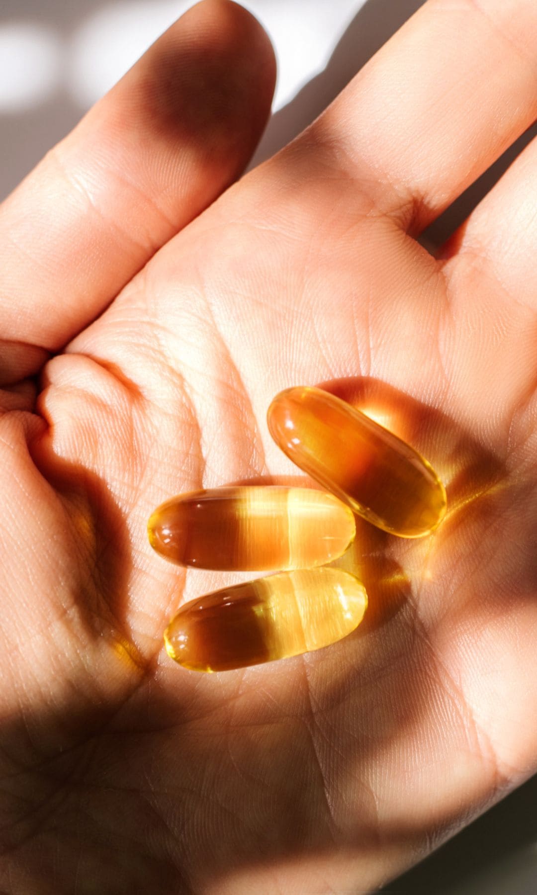 Mano de mujer sosteniendo tres perlas de suplementos alimenticios.