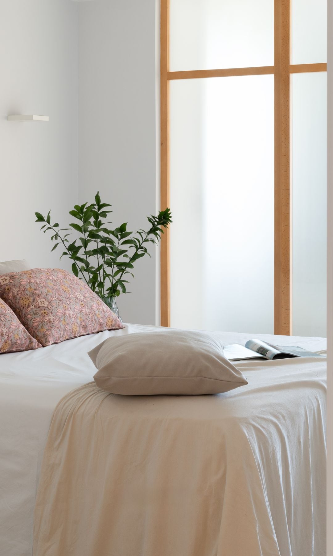 Dormitorio con ventilador de techo blanco, planta al lado de la cama, cojines, ropa de cama y revista sobre la cama