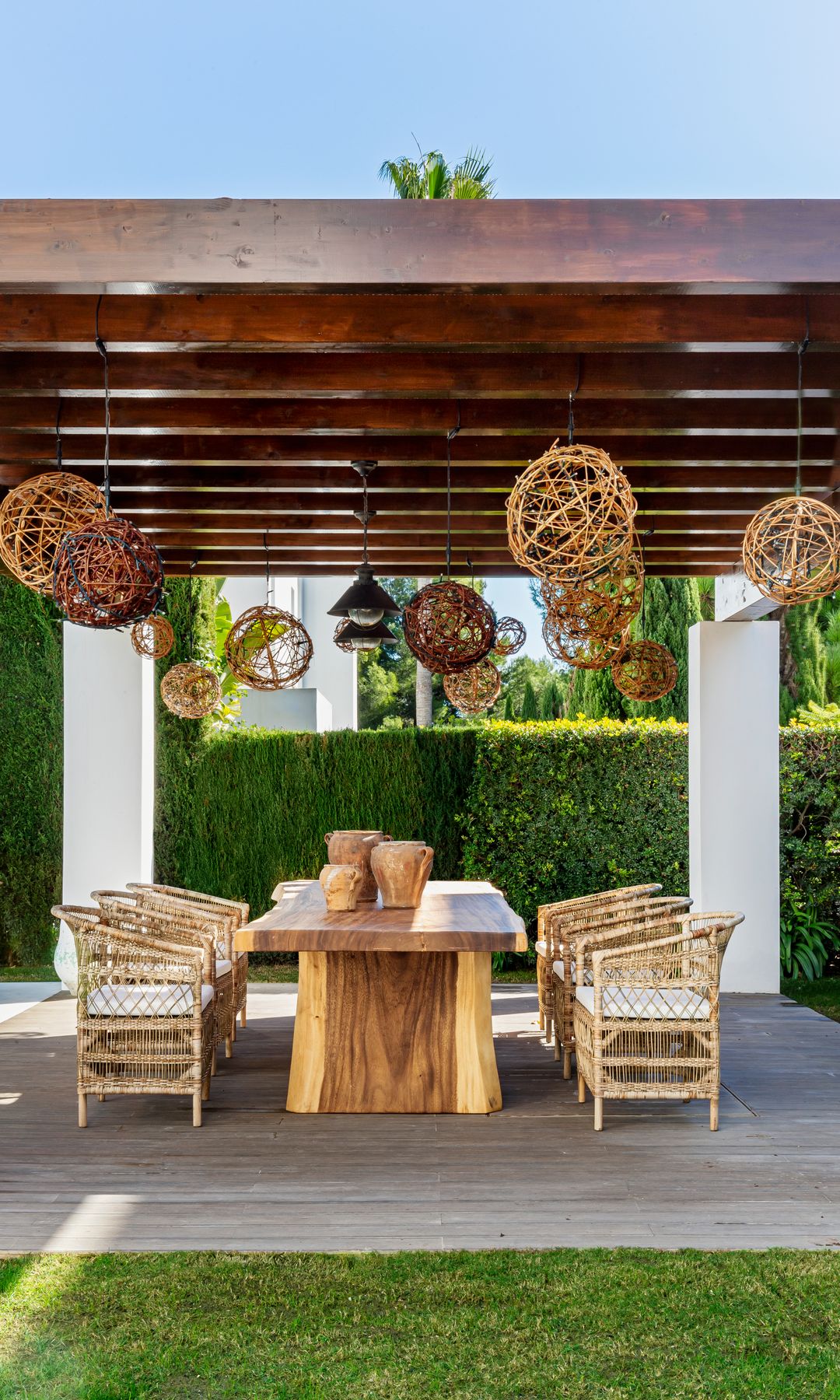 Pergola de madera con comedor de madera con sillas de fibras naturales y lámparas de techo de fibras vegetales