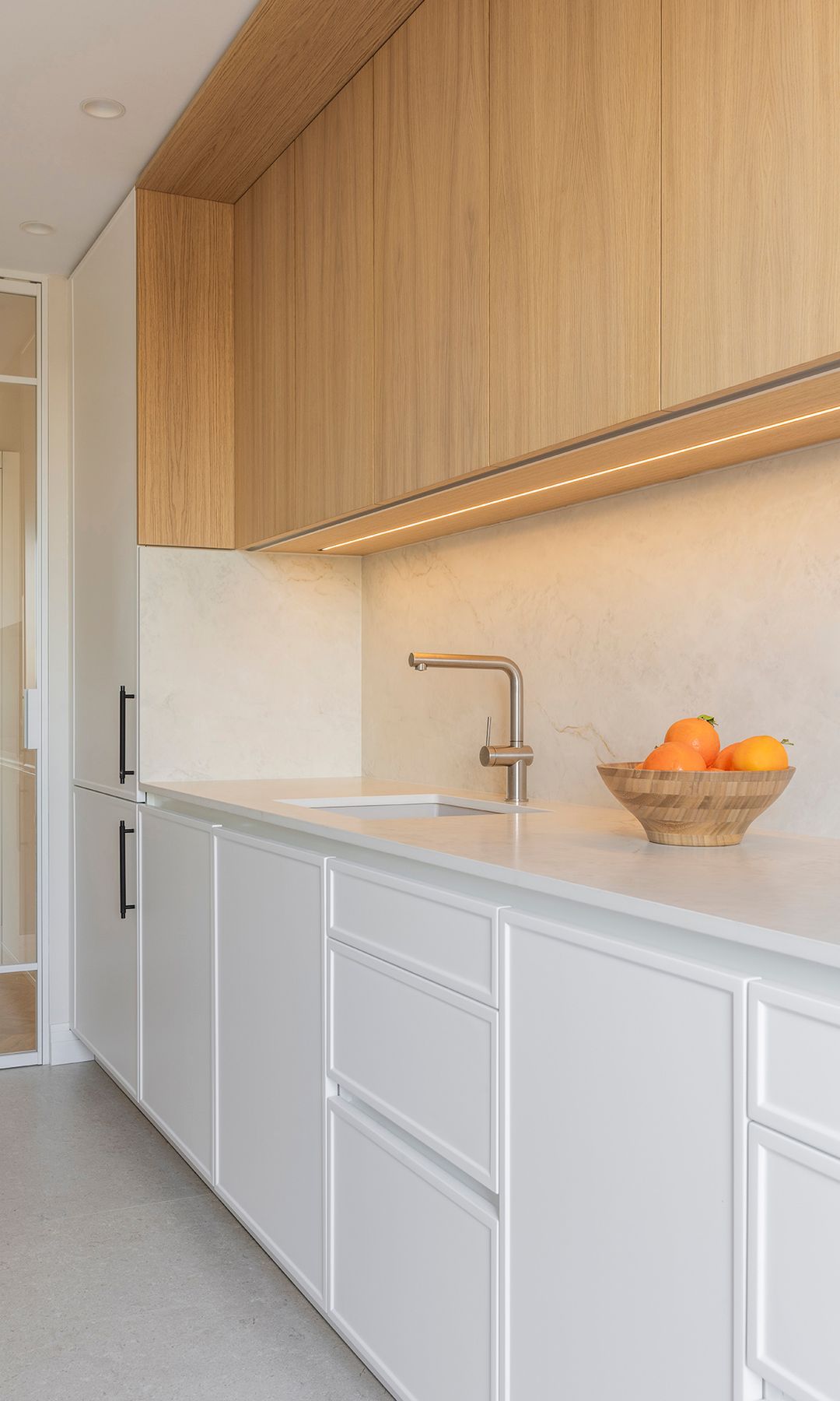 Cocina blanca y de madera con tira led bajo los armarios superiores, encimera blanca, frutero de bambú 