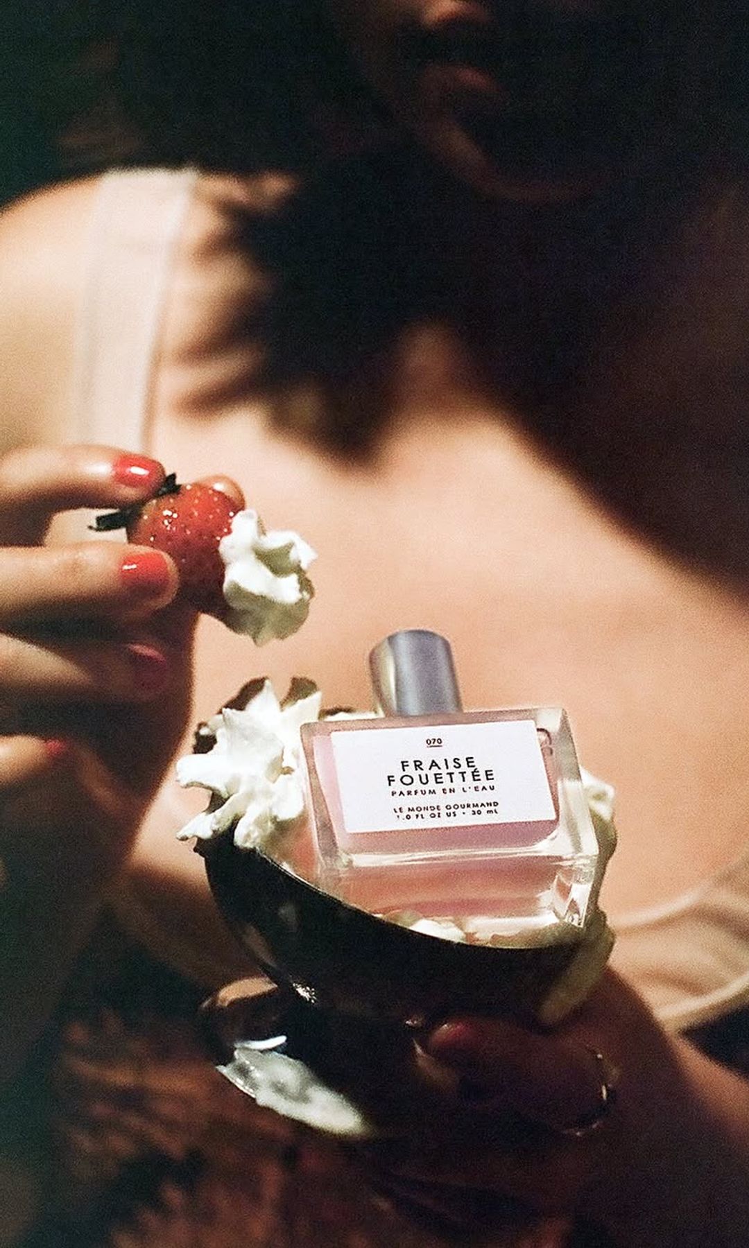 Frasco del perfume Fraise Fouettée, de Le Monde Gourmand, acompañado de fresas y nata, una composición que evoca el universo de las fragancias gourmand