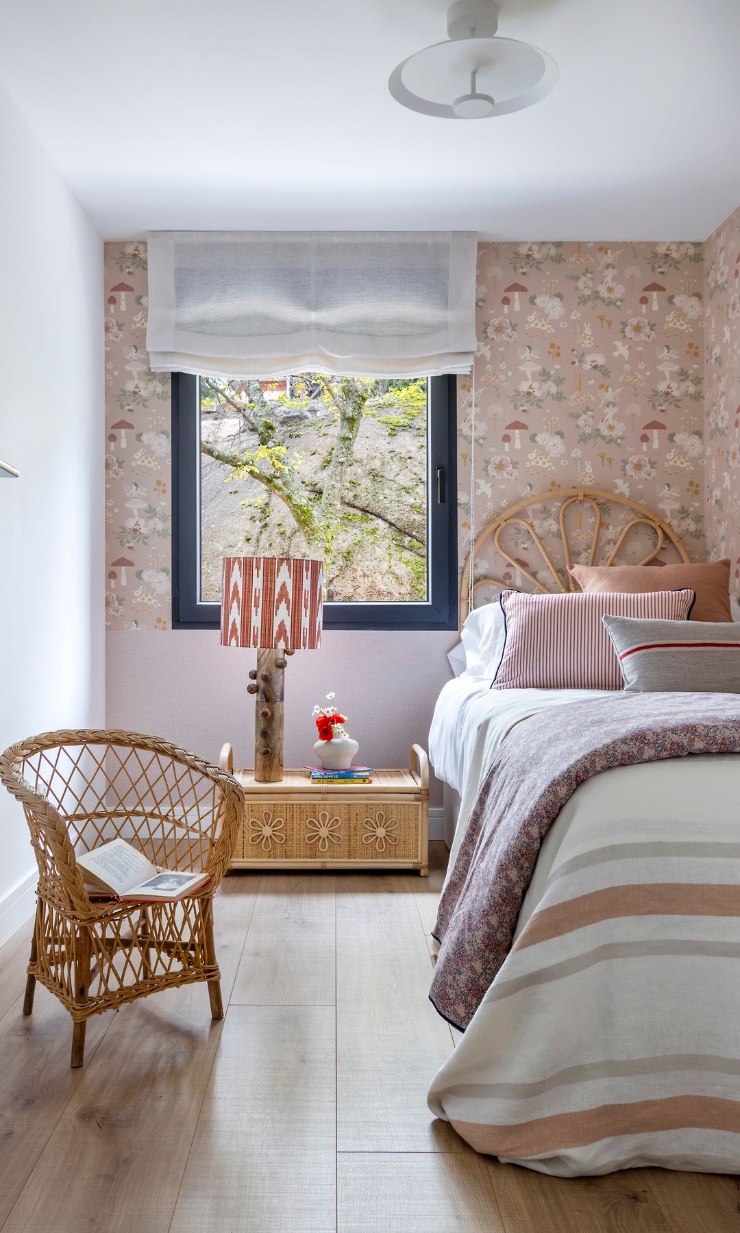 Habitación infantil con papel pintado, cabecero de fibras vegetales, lámpara de sobremesa, estor blanco, butaca de fibras vegetales