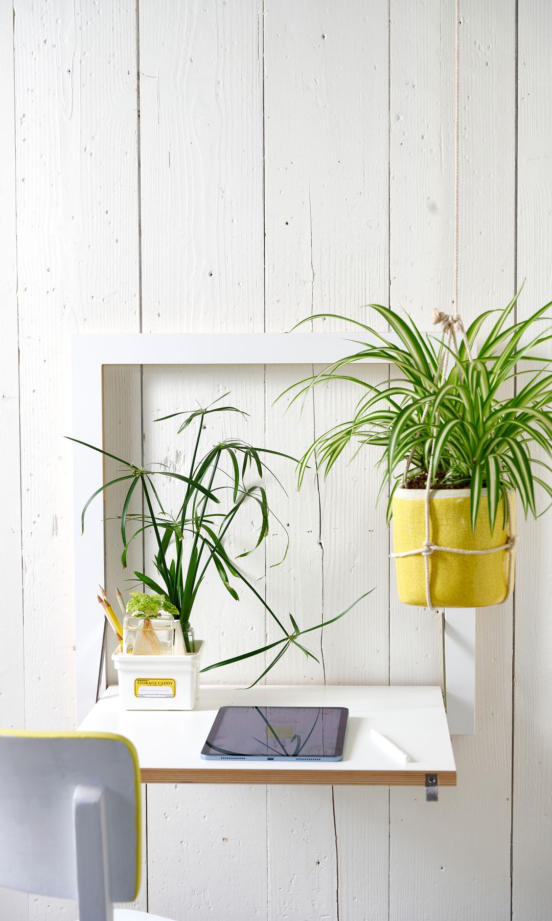 Pared de lamas de madera blanca, macetero amarillo y cinta, balda escritorio, tablet y silla