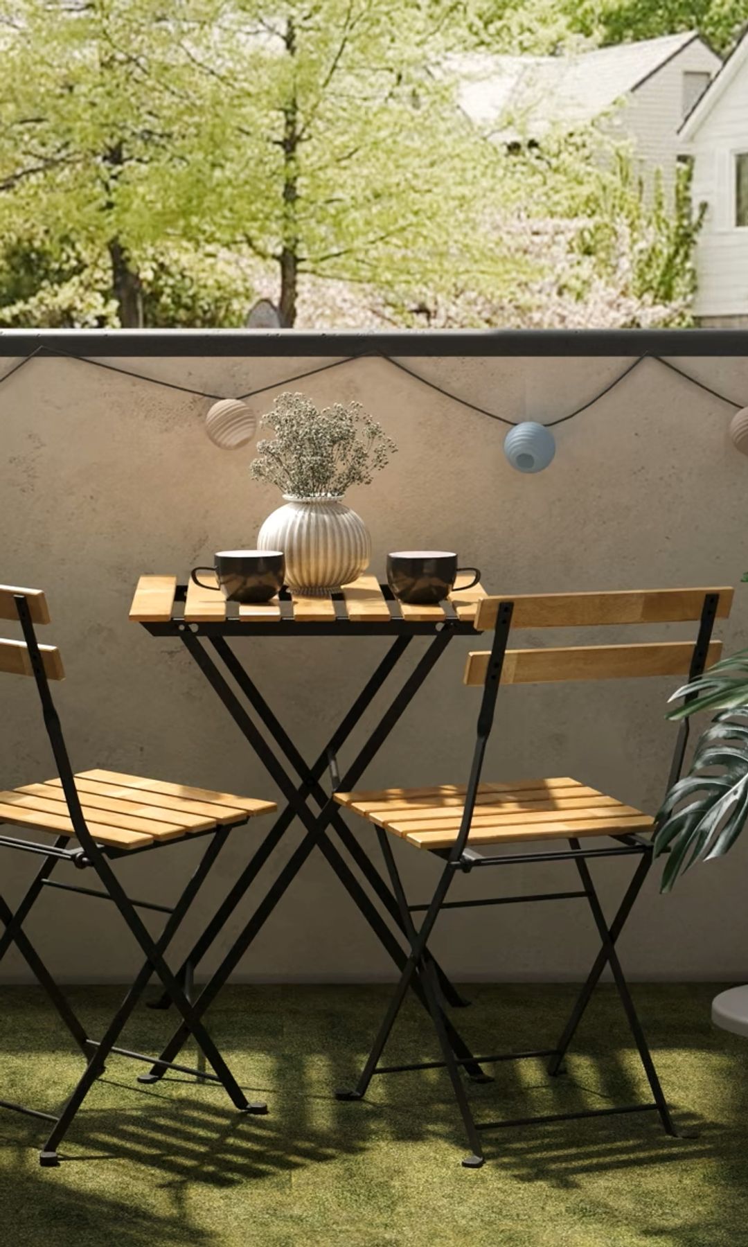 Balcón con muebles plegables de hierro y madera, guirnalda de luz por la pared, césped artificial 