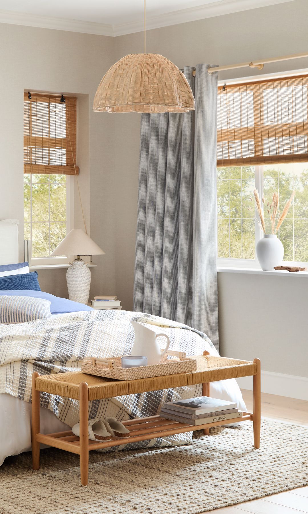 Dormitorio con cabecero tapizado en blanco, banco a los pies de la cama, estores enrollables de fibras vegetales, lámpara de fibras vegetales, alfombra 