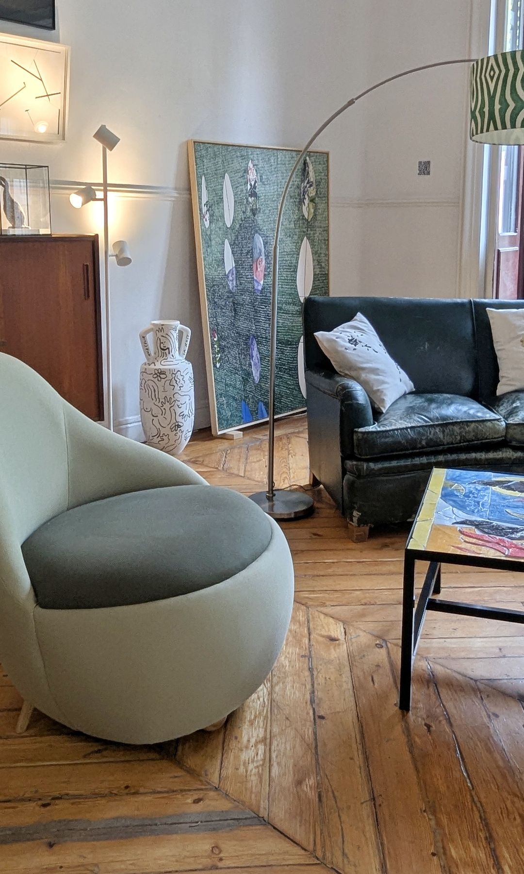 Salón con butaca verde, mesa de centro metálica, lámpara de pie, suelo de madera antiguo, mueble bar, cuadro en la pared