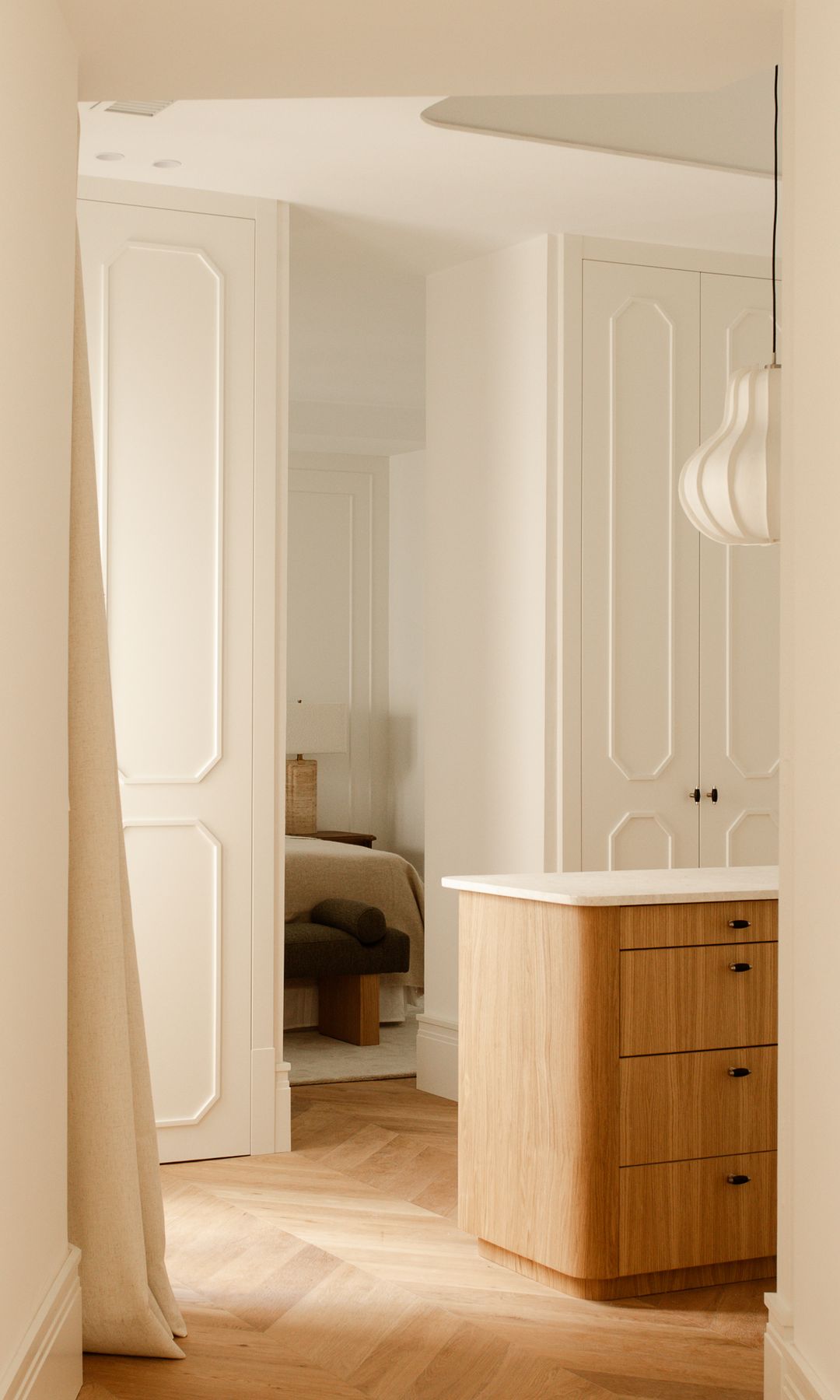 Vestidor con cómoda de madera en el centro, armarios lacados con molduras, lámpara de techo blanca 
