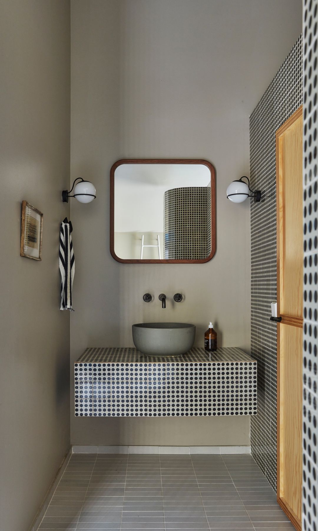 Baño con encimera de gresite en blanco y negro, apliques de pared negro, lavabo redondo sobre la encimera, grifería negra