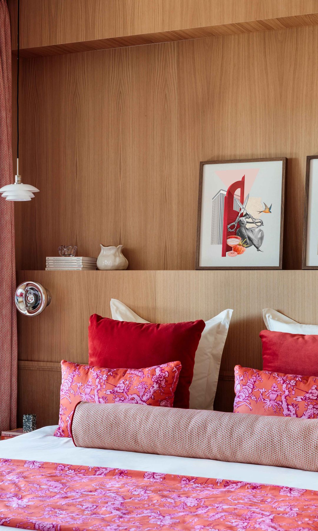 Dormitorio con pared del cancero y cabecero de madera, cojines y ropa de cama de color rojo y morado, cabecero con balda y cuadros sobre ella, cortinas