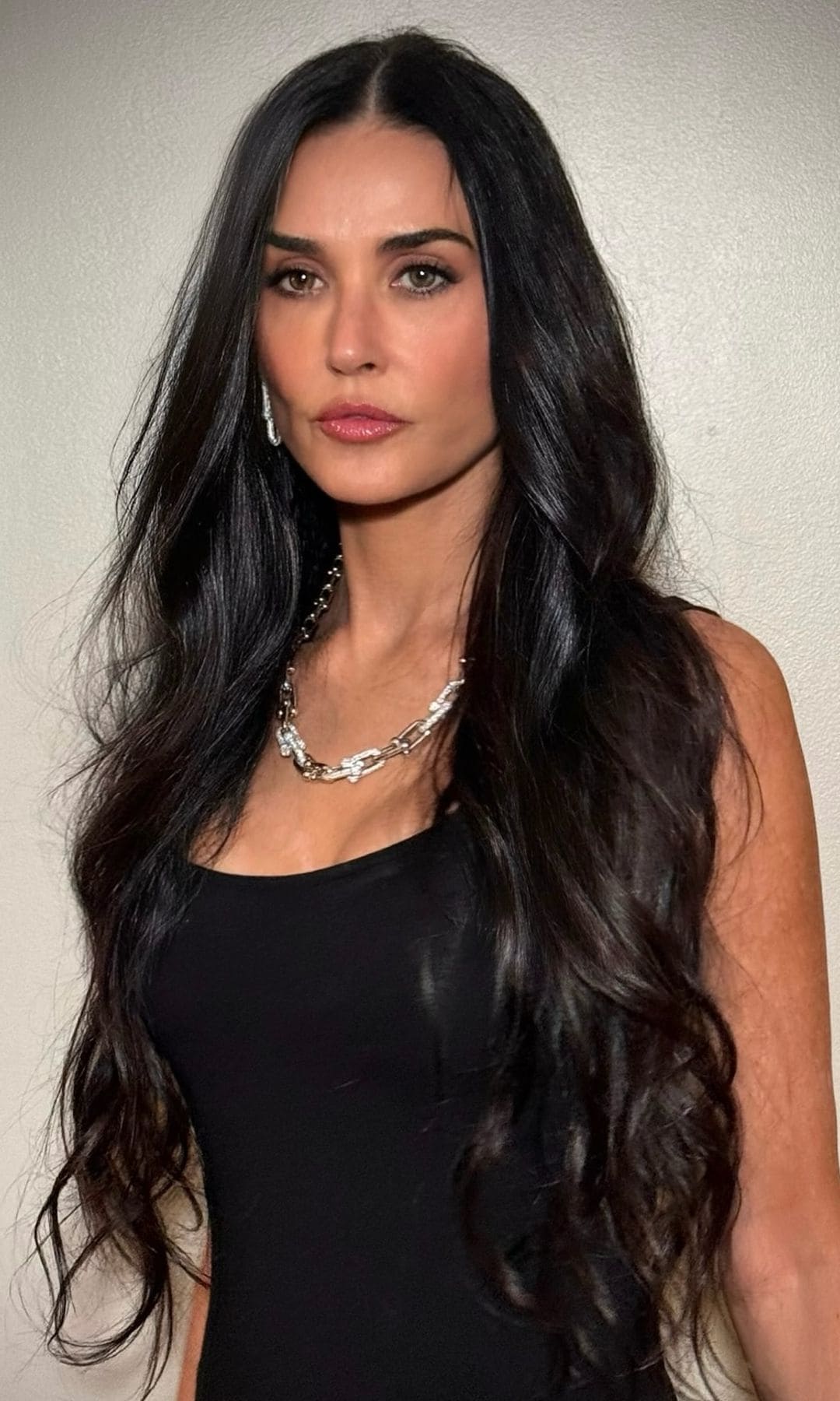 Demi Moore con vestido negro, pelo suelto y fondo neutro