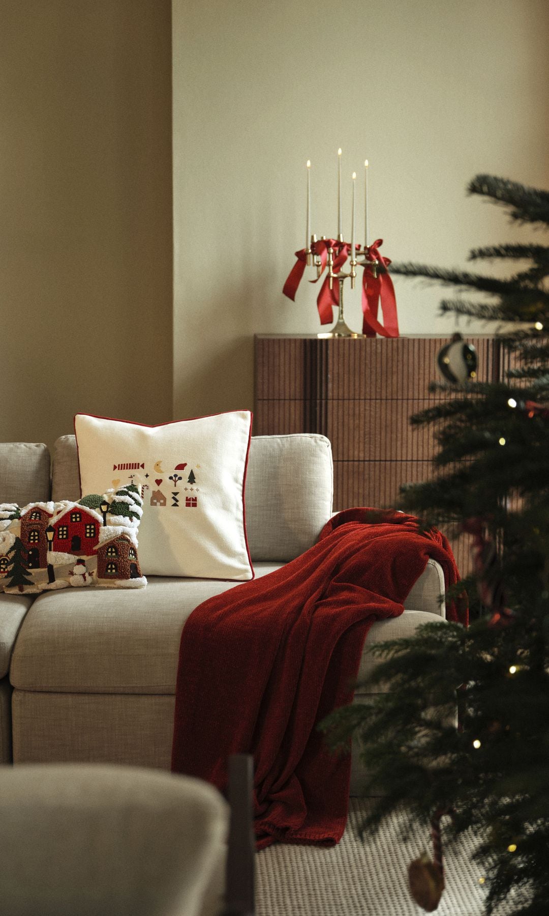 Decoración Navidad, con cojines con motivos navideños, árbol de Navidad, manta roja, candelabros con lazos rojos, sofá beige