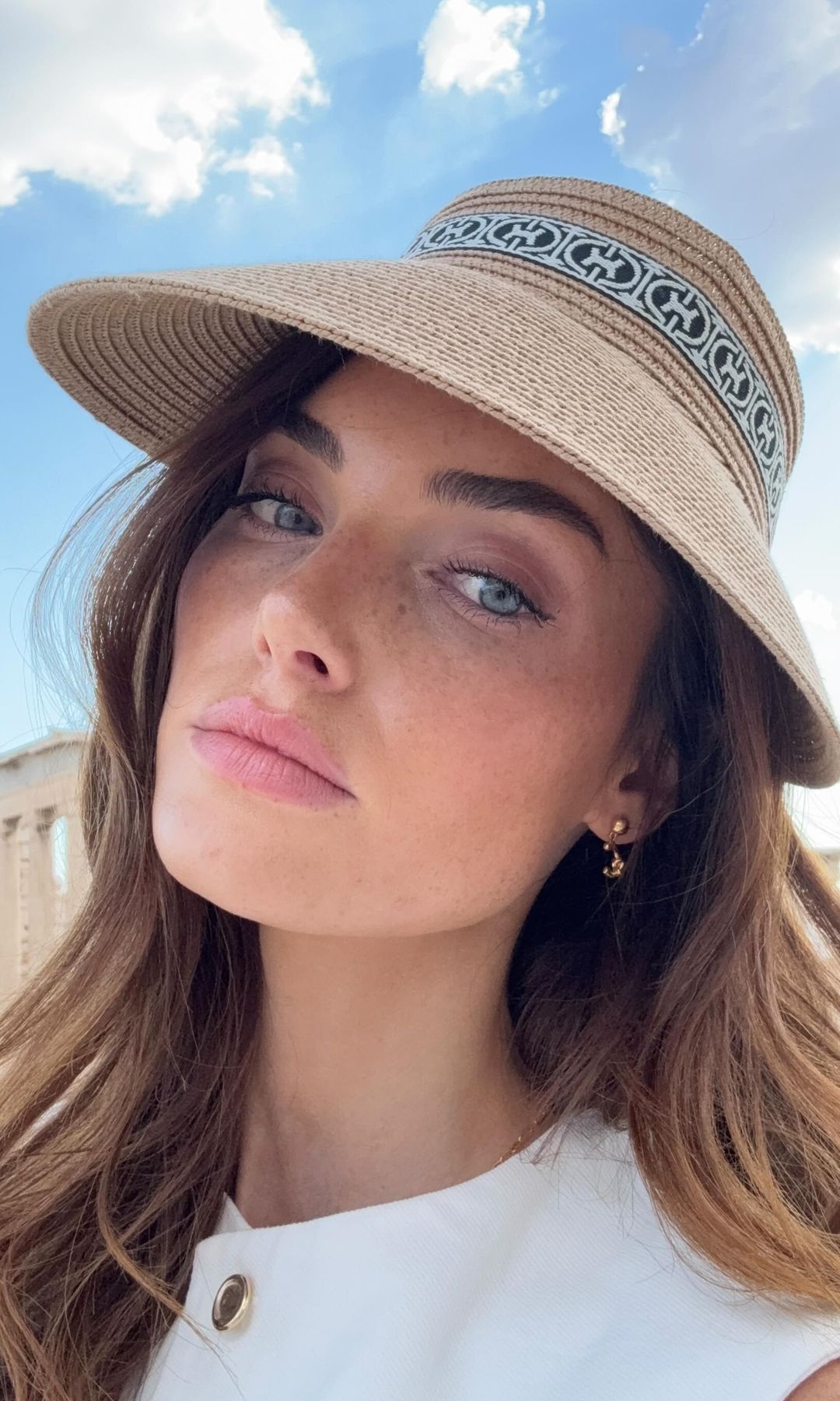Mujer con sombrero de ala ancha posa al sol con el cielo azul de fondo