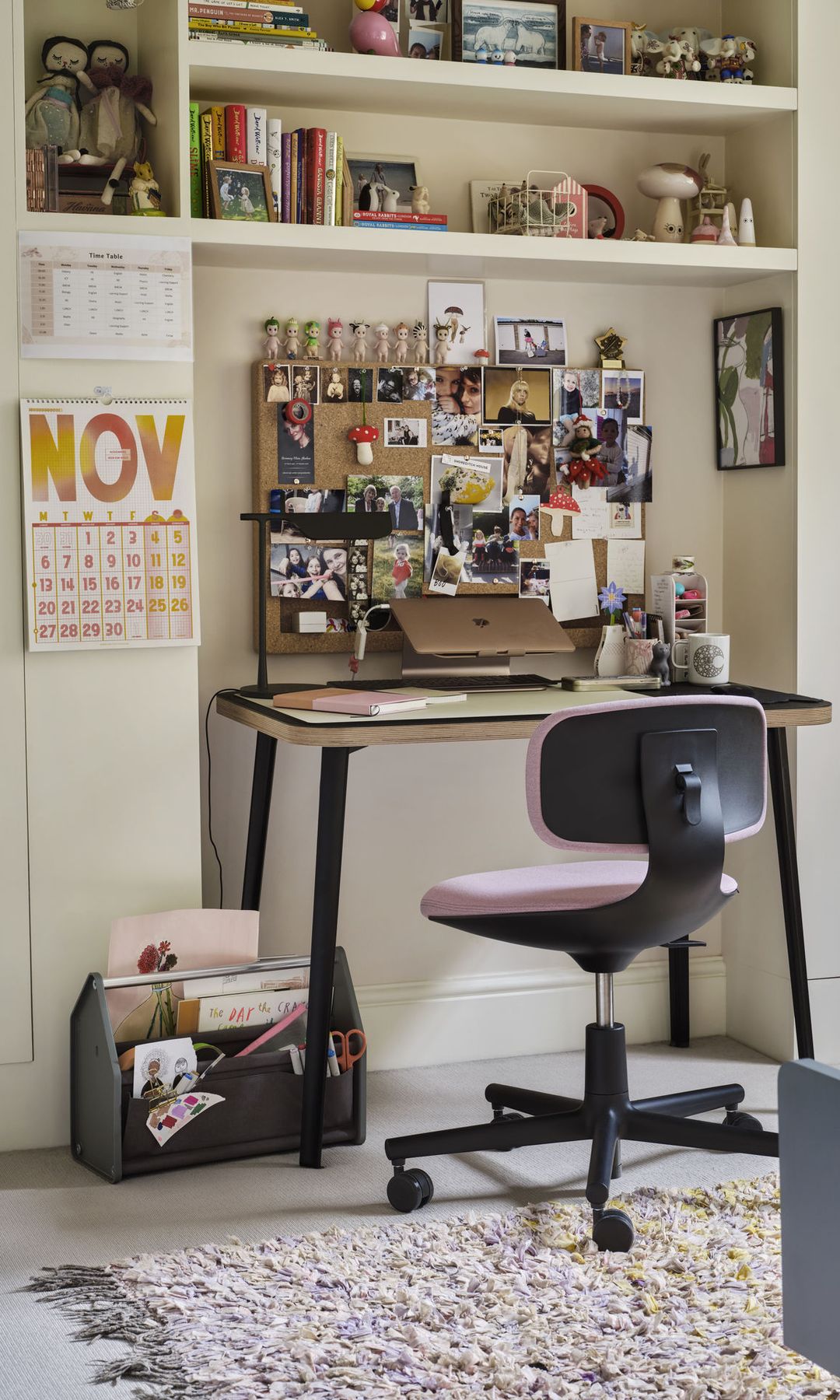 Escritorio con corcho con fotos y notas, mesa de escritorio, silla de oficina con ruedas de color rosa, revistero de madera, baldas, adornos y objetos