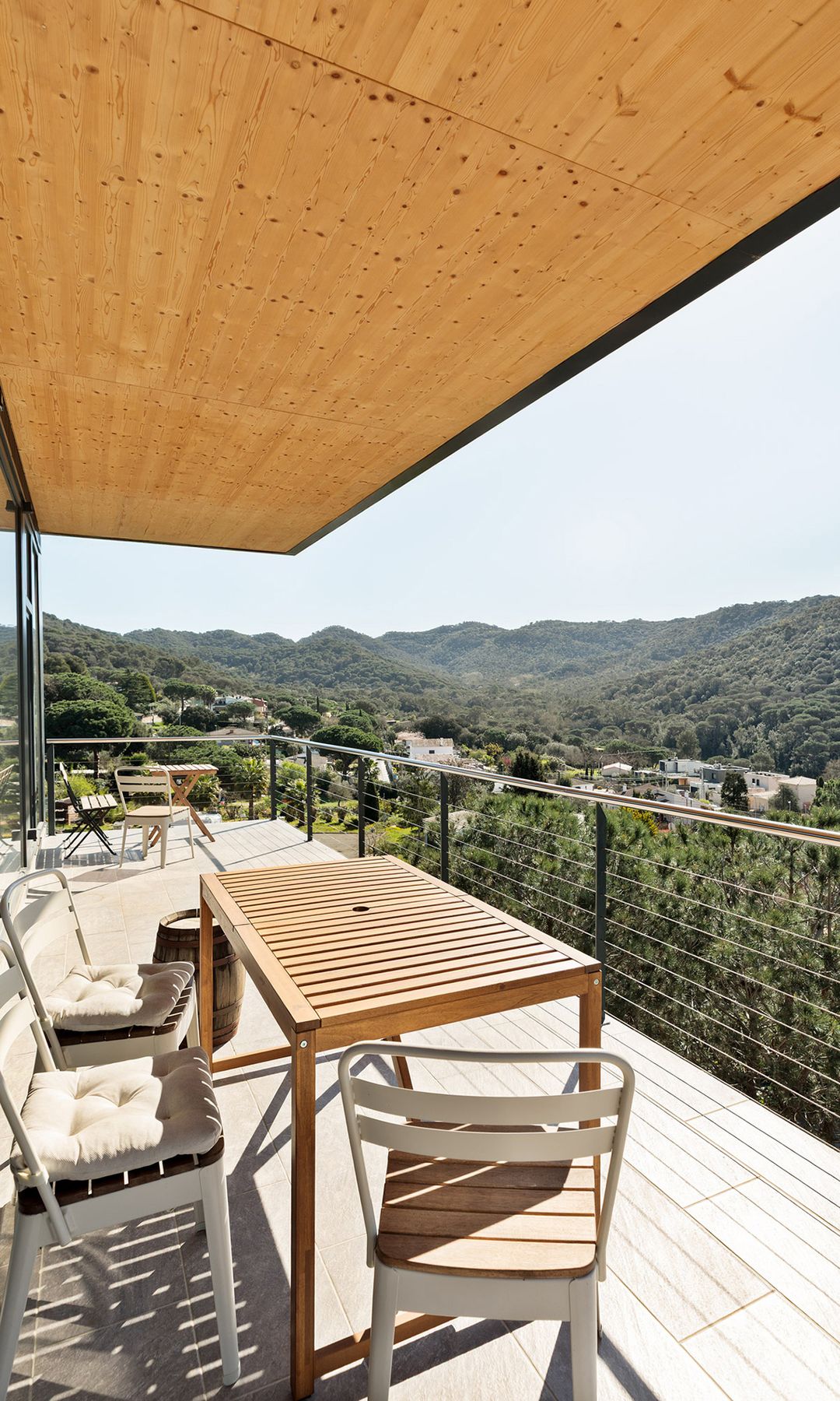 Terraza con vistas a un bosque con suelo y techo de madera, mesa de madera y sillas blancas 