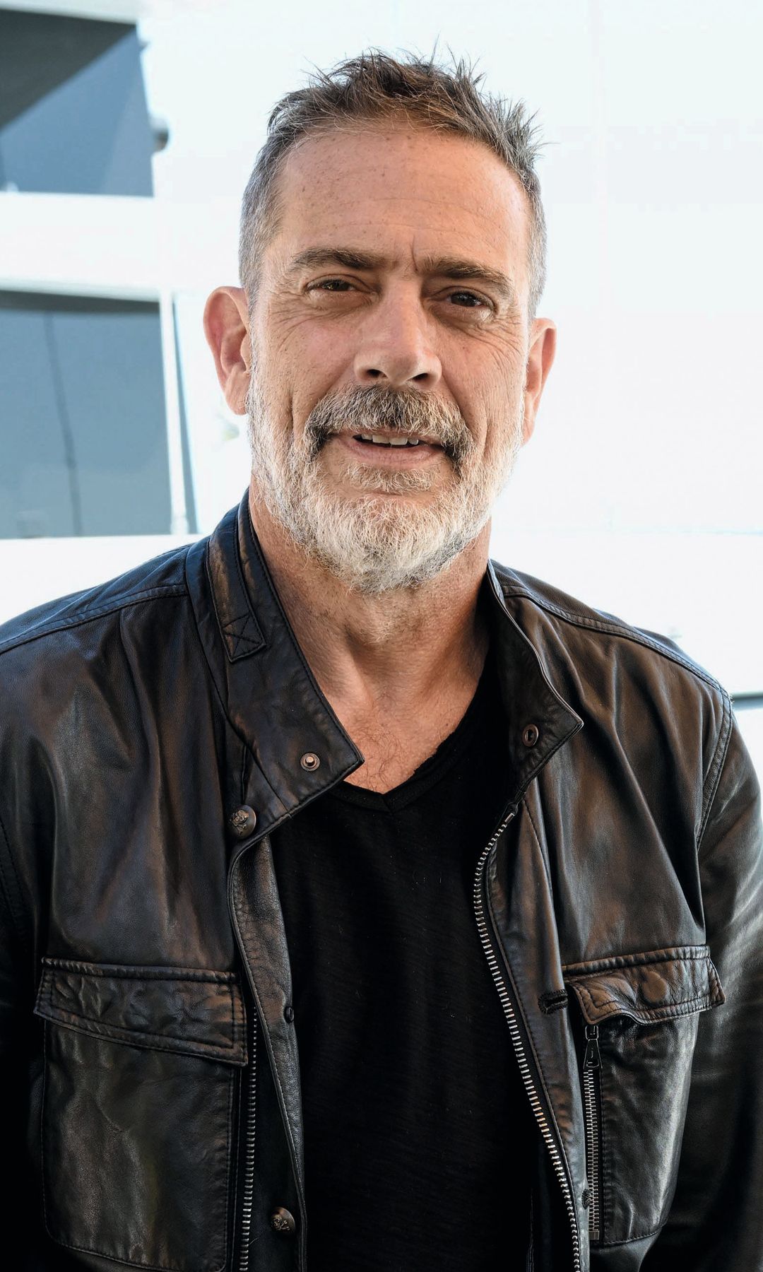 Jeffrey Dean Morgan, con barba y bigote, viste chaqueta de cuero negra y camiseta negra.