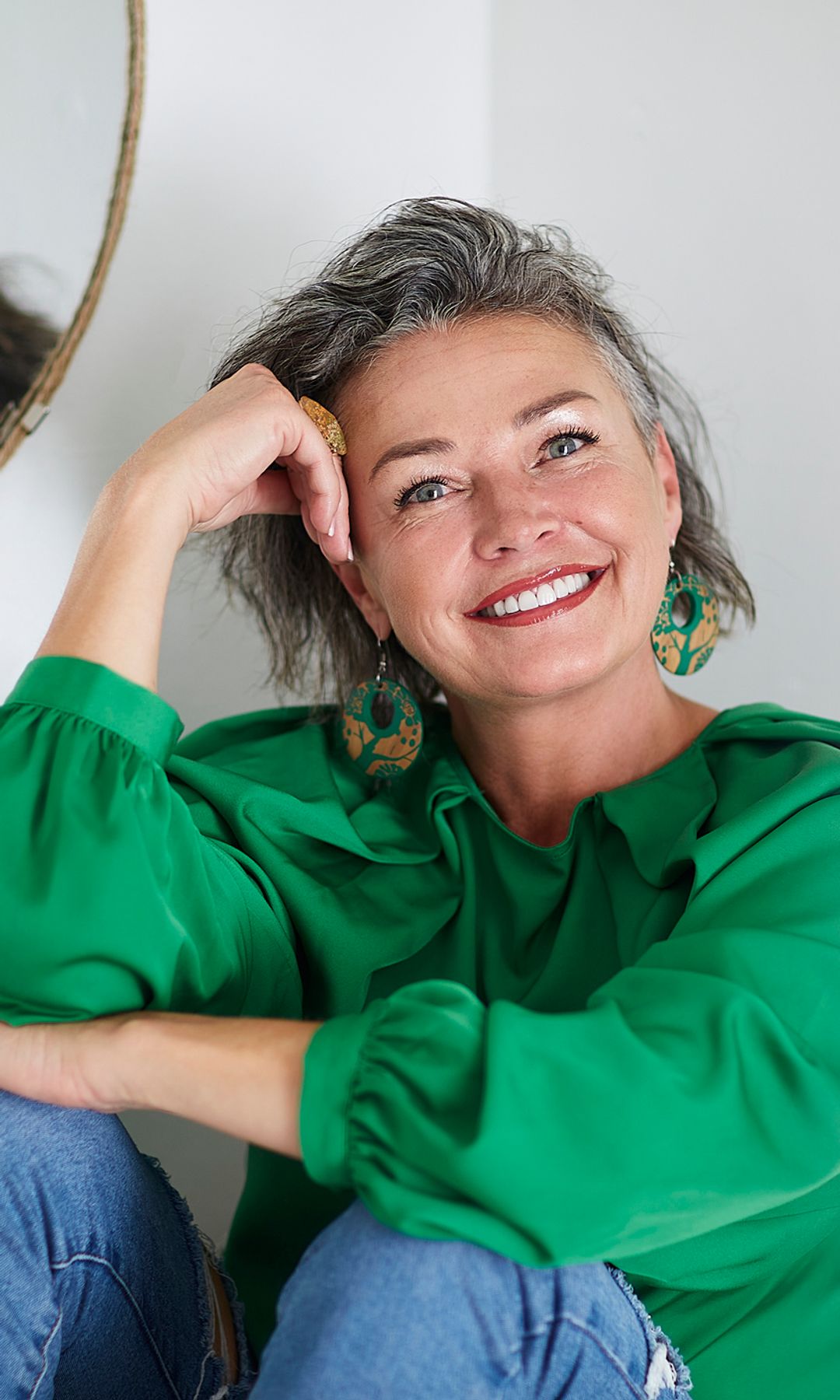mujer madura y sonriente con una camisa verde mirando a cámara