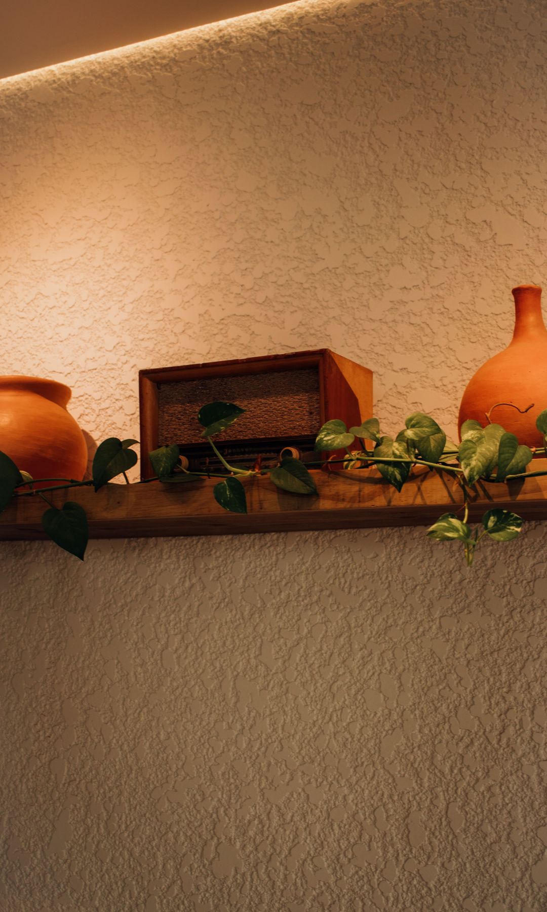 Pared con gotelé, iluminación en el techo, balda de madera con accesorios de barro
