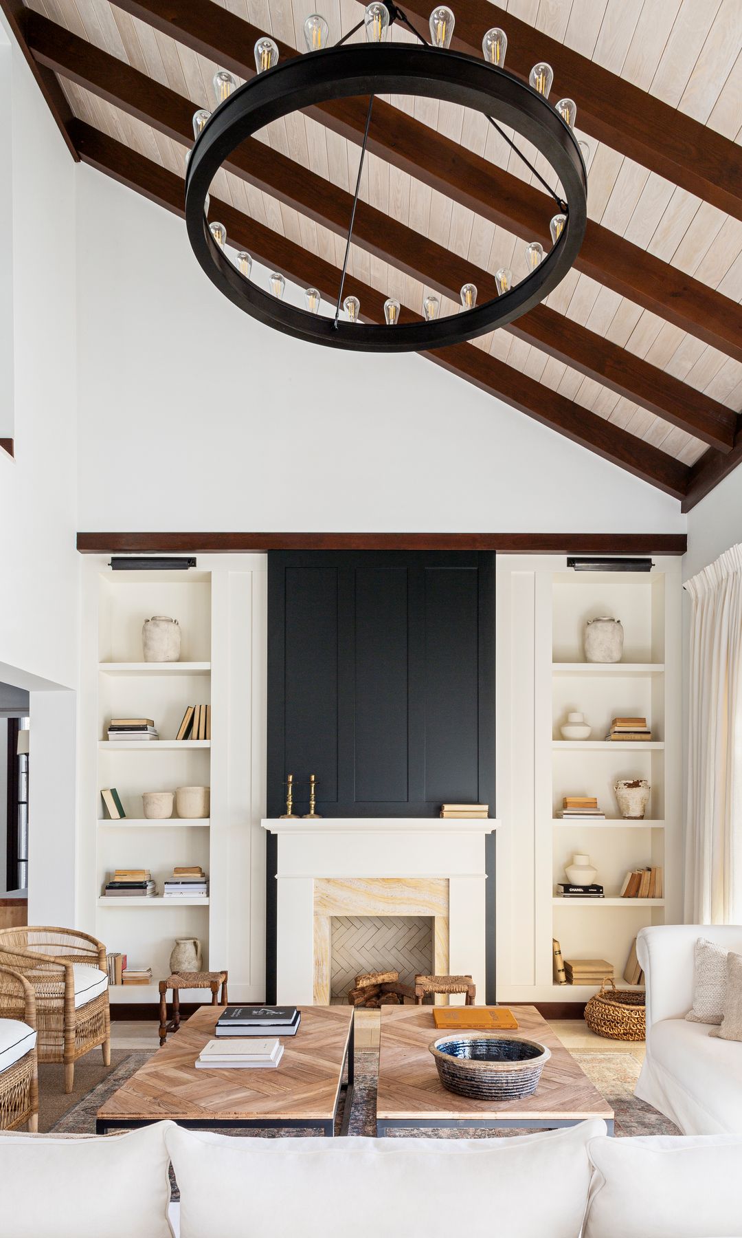 Salón con chimenea, lámpara de techo tipo castillo de madera, estanterías a los lados de la chimenea, sofás blancos, mesas de centro con el sobre de madera, butaca de fibras vegetales