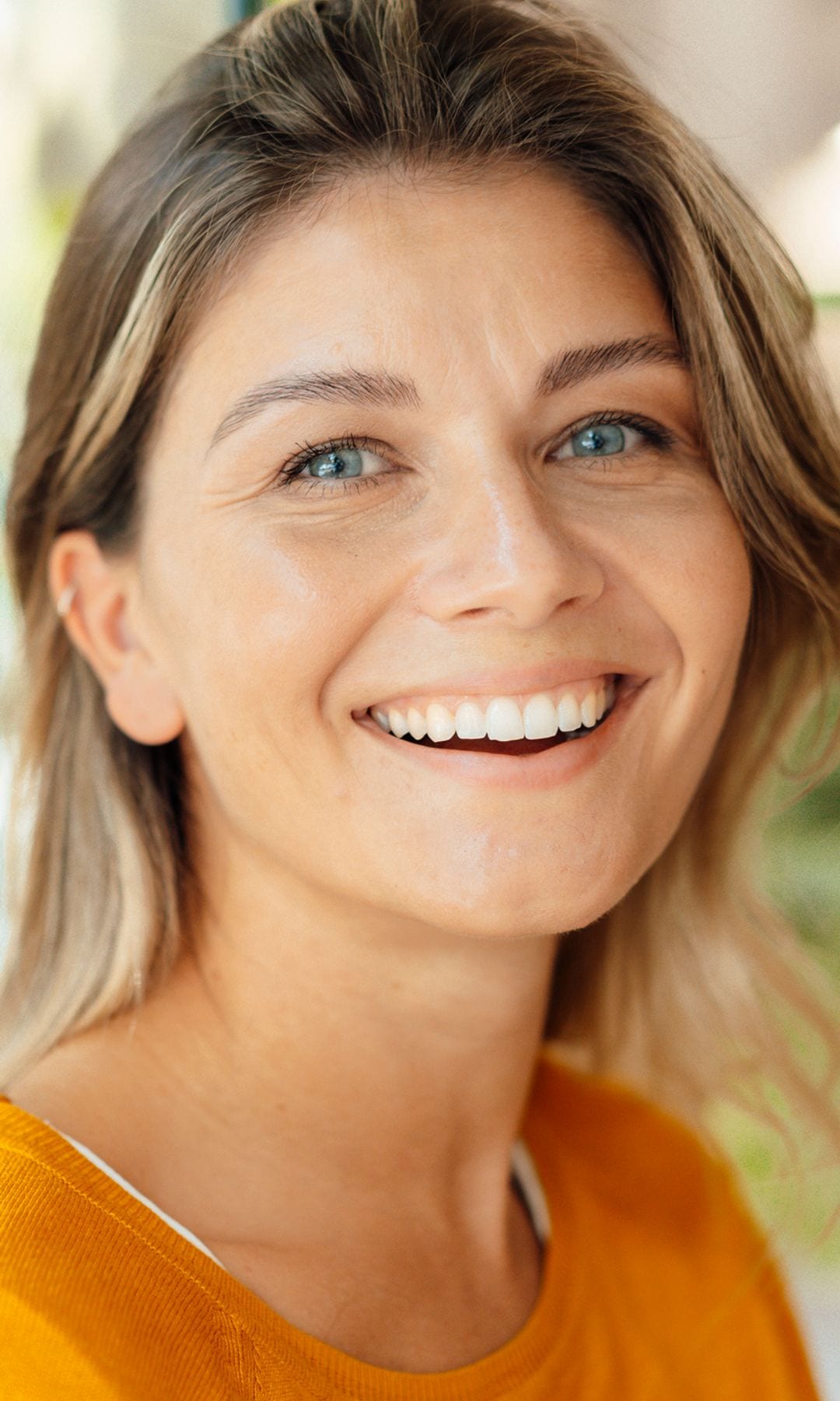 Mujer sonriendo en primer plano con cabello rubio y ojos azules, sonrisa.